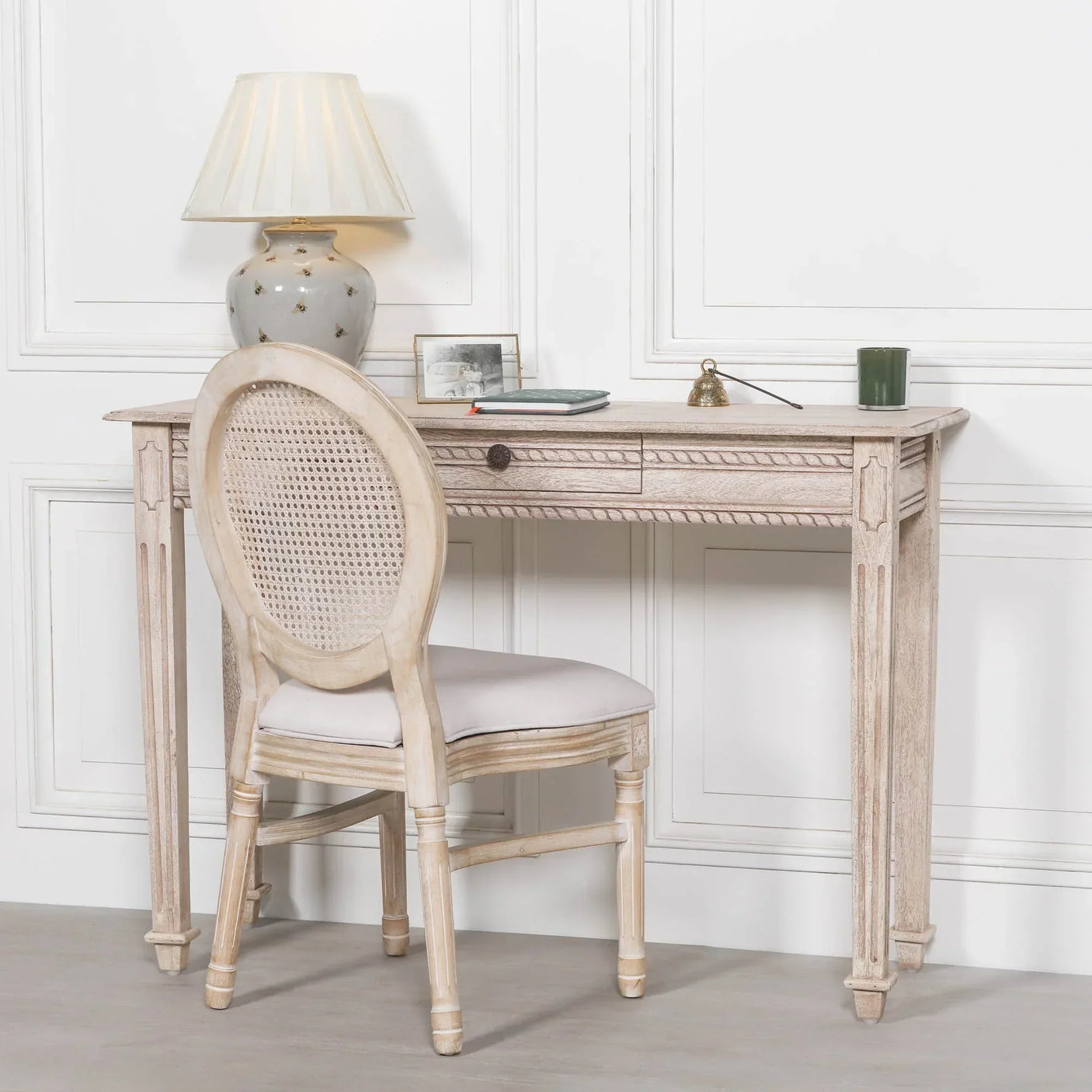 Rustic wooden writing desk with cane back chair and table lamp in a white painted room