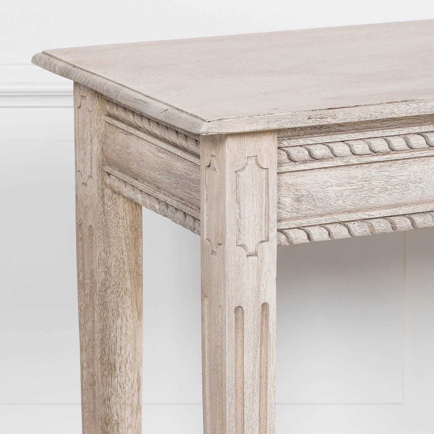 Light wood console table with carved detailing on leg and decorative edge, side angle view