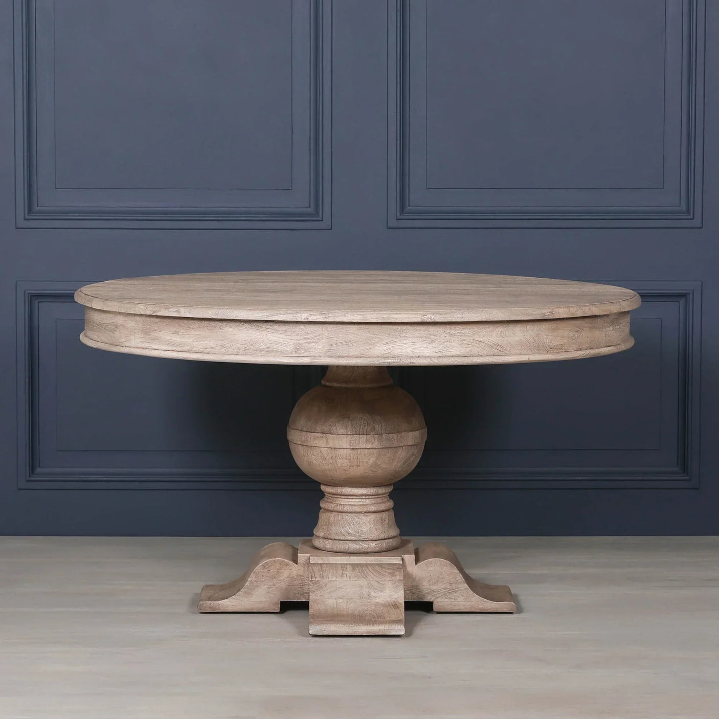 Round wooden dining table with pedestal base against dark wall panel backdrop