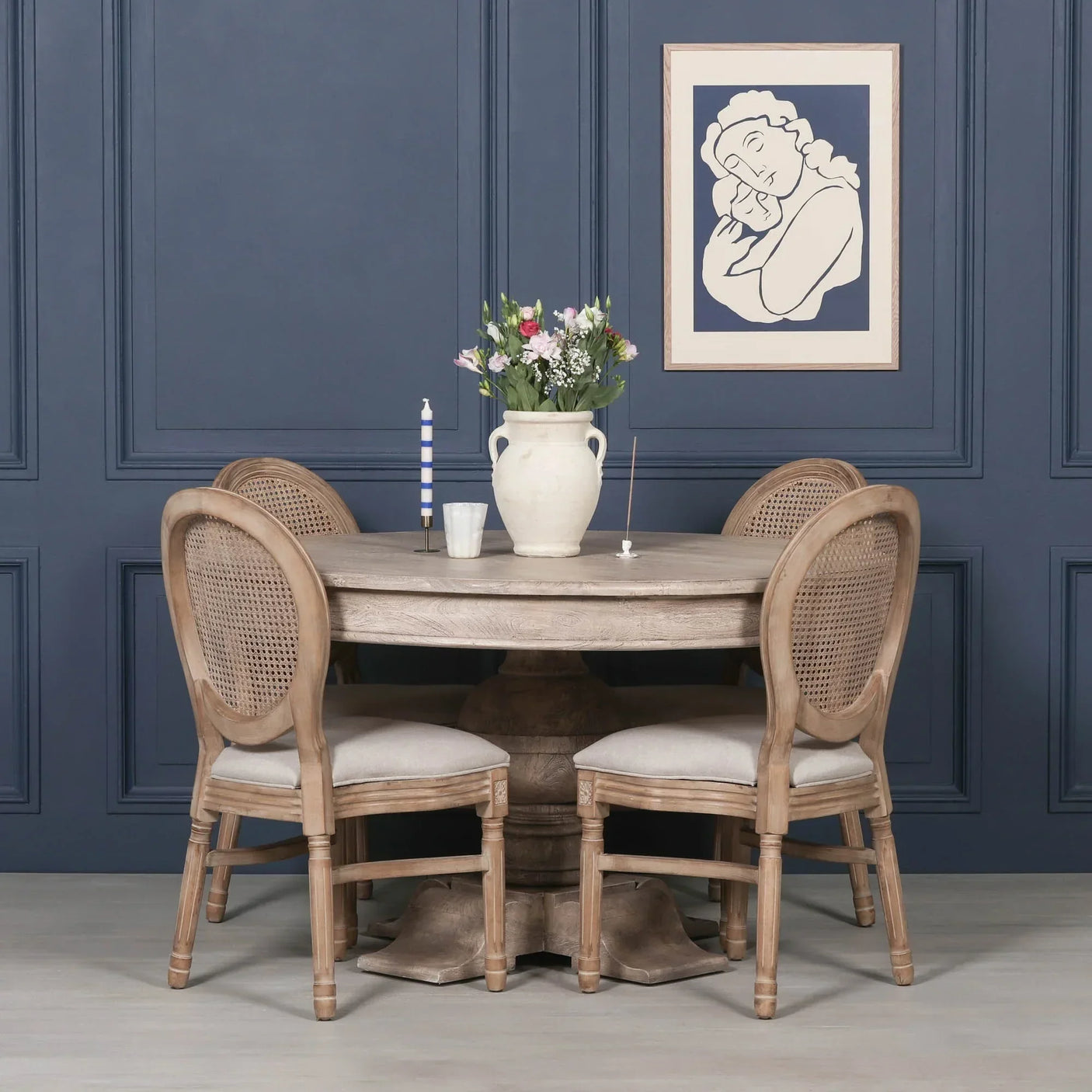 Round wooden dining table with four upholstered rattan back chairs against blue paneled wall