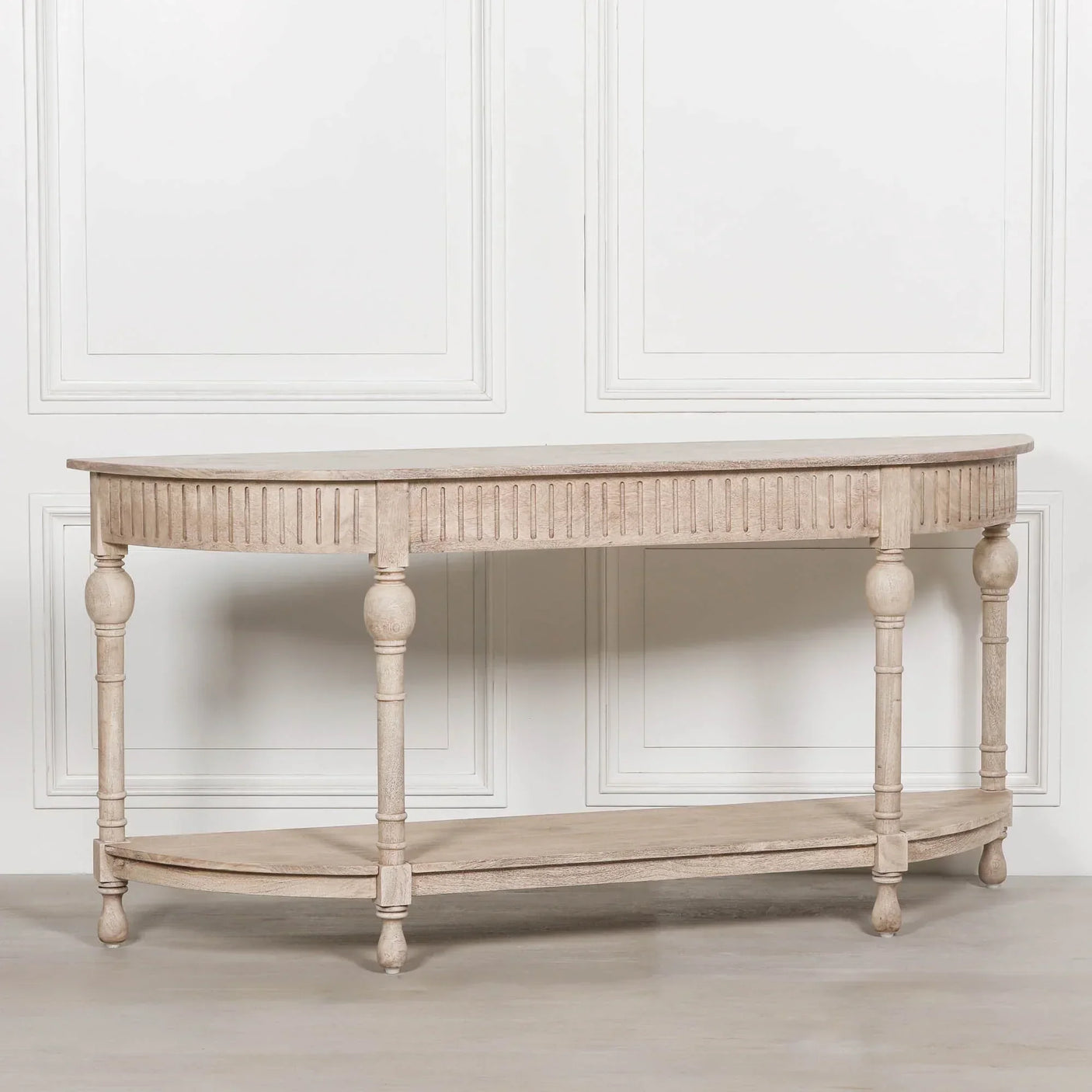 Light wood console table with fluted apron and lower shelf against white panel wall