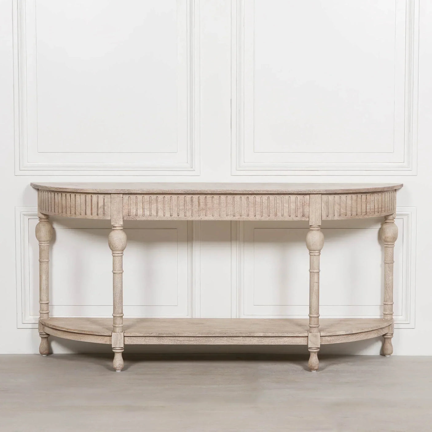 Light wood console table with carved legs and lower shelf against white panel wall