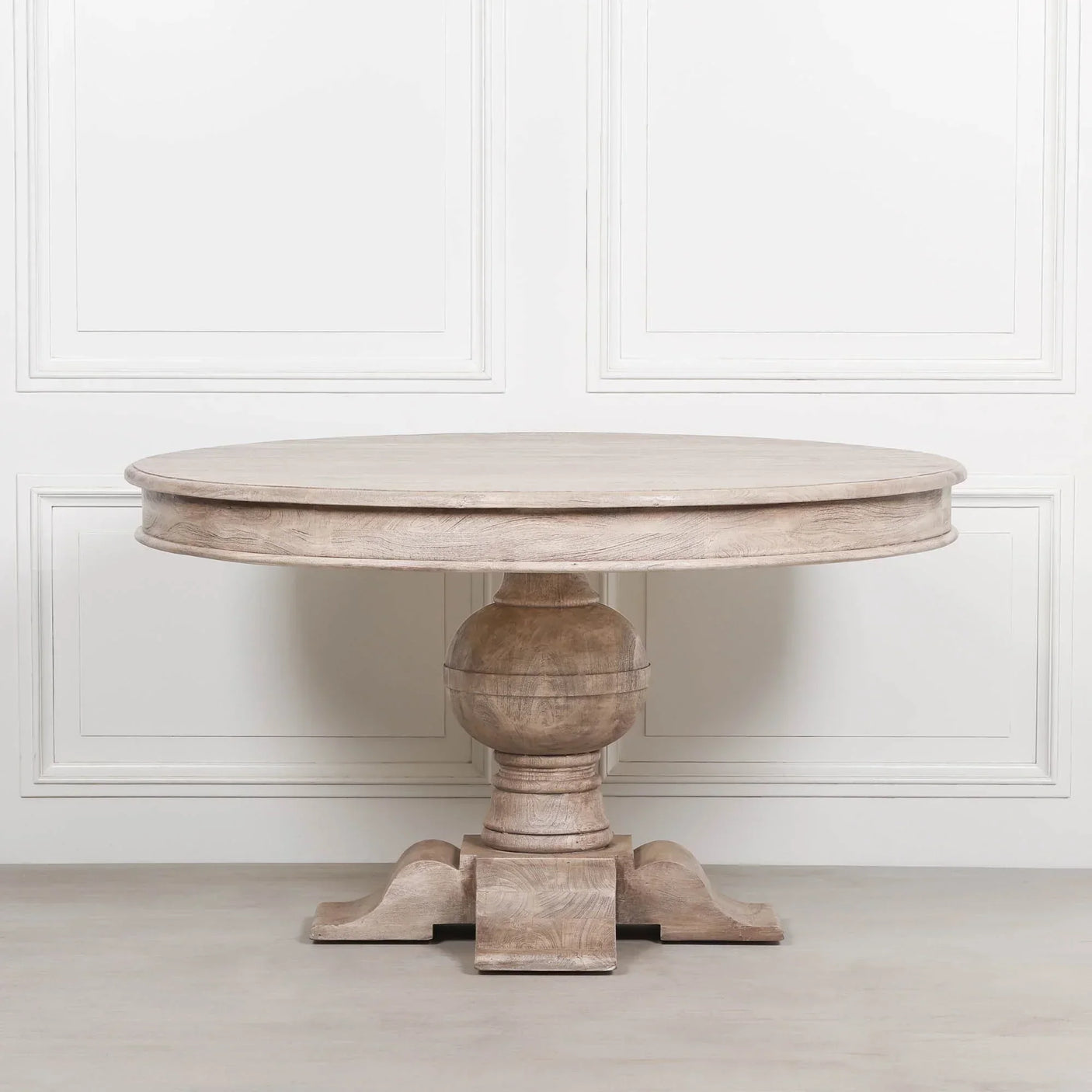 Round wooden dining table with thick pedestal base and natural finish on light floor