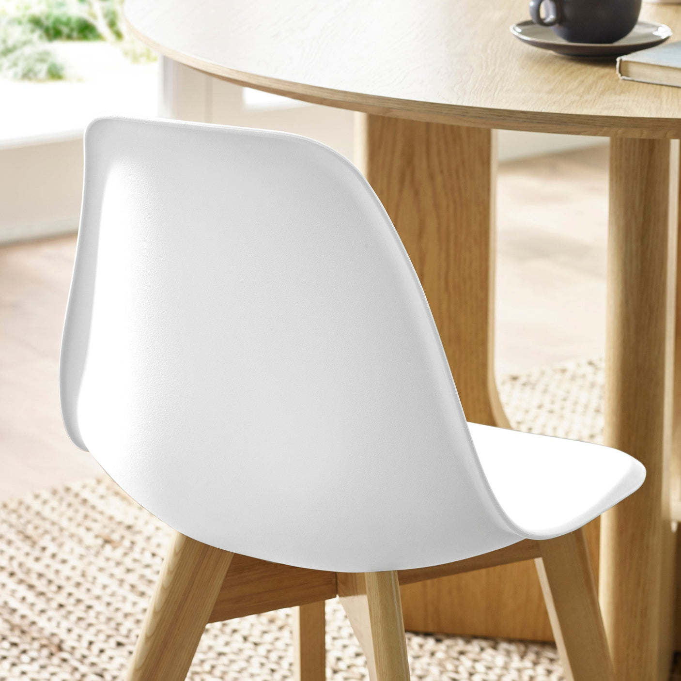 Close-up of white plastic chair backrest and natural wood legs beside oak dining table and woven rug