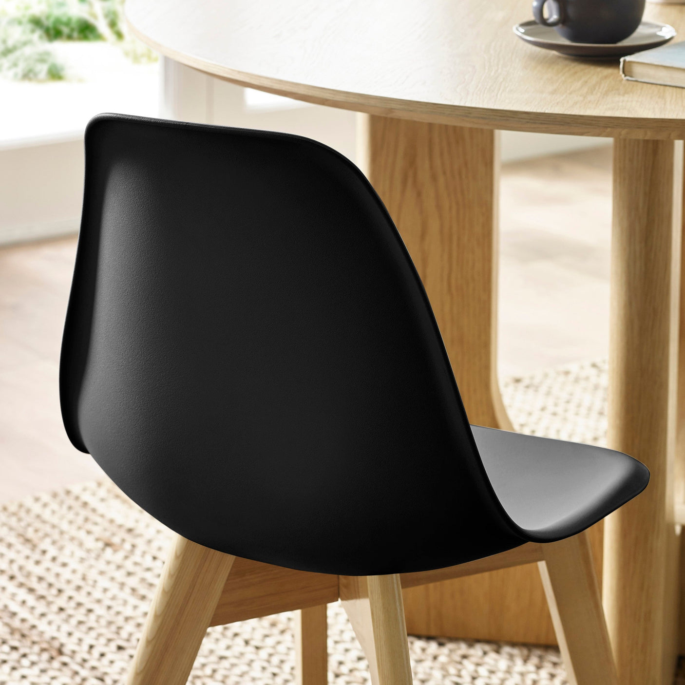 Back view of black plastic seat with natural wood legs, set near light wood dining table on rug.