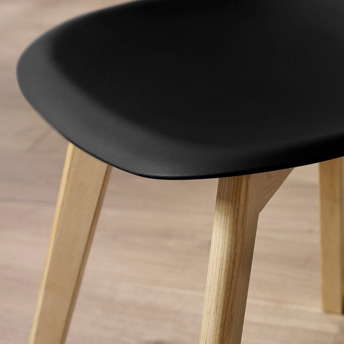 Close-up showing black seat edge and textured light wood legs on wooden floor.