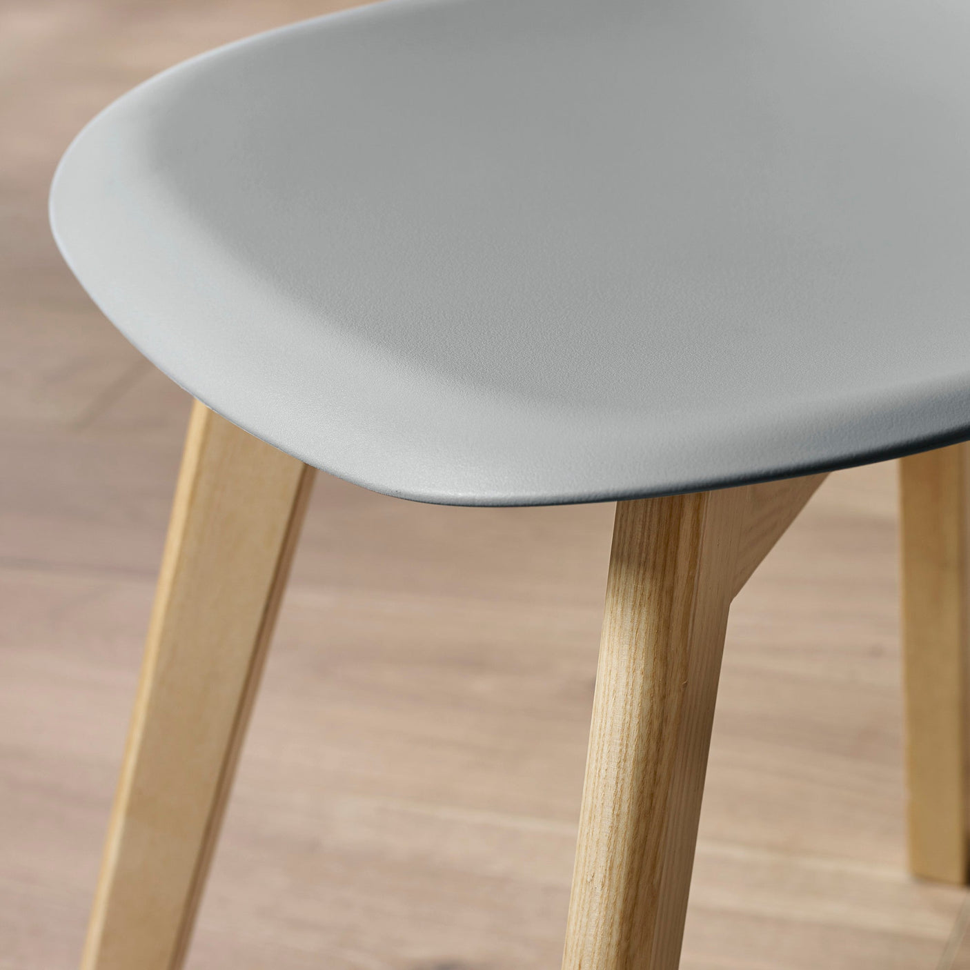 Close-up detail of grey molded seat edge and natural wood chair leg on wooden floor