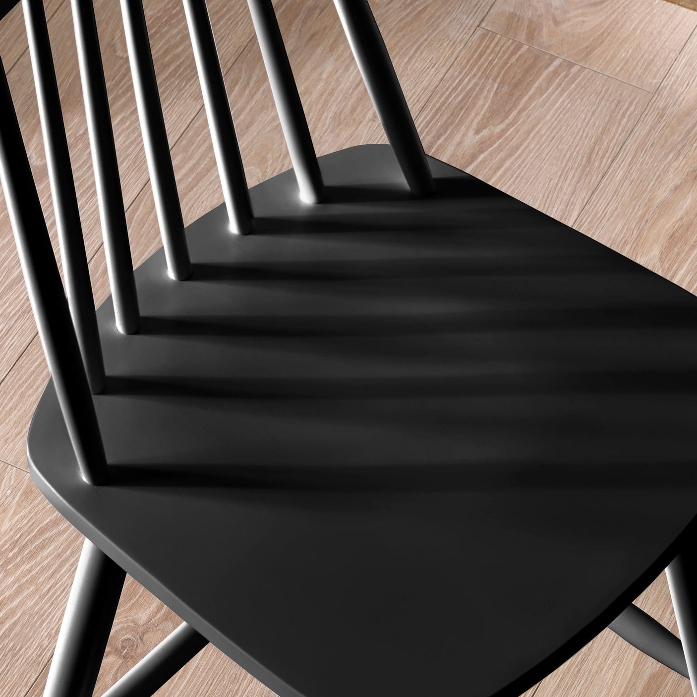 Close-up of black wooden bar stool seat and spindle back detail on light wood floor.
