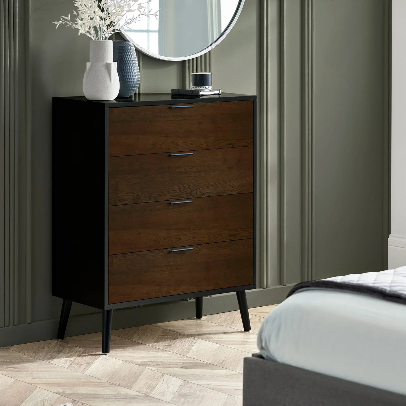 Walnut and black 4 drawer chest with slim legs beside bed in modern bedroom