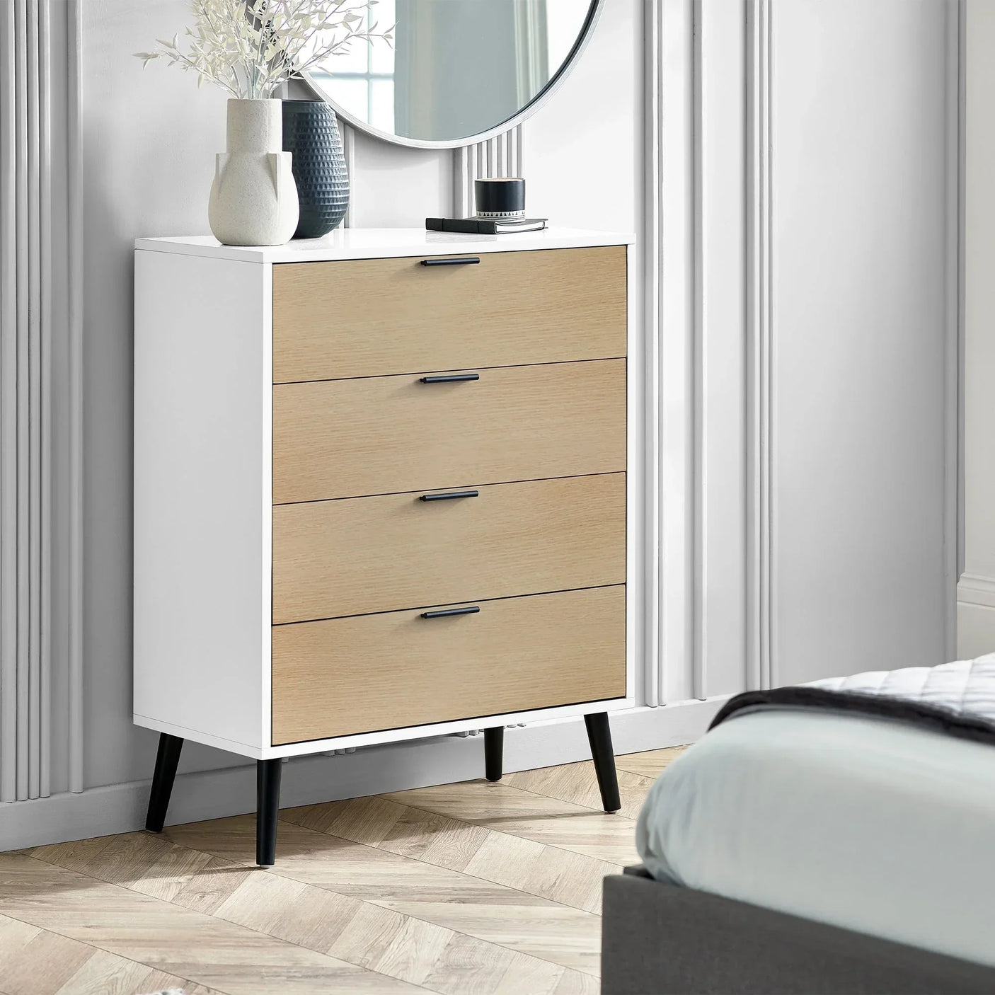 White and oak four drawer chest with black handles in modern bedroom next to bed
