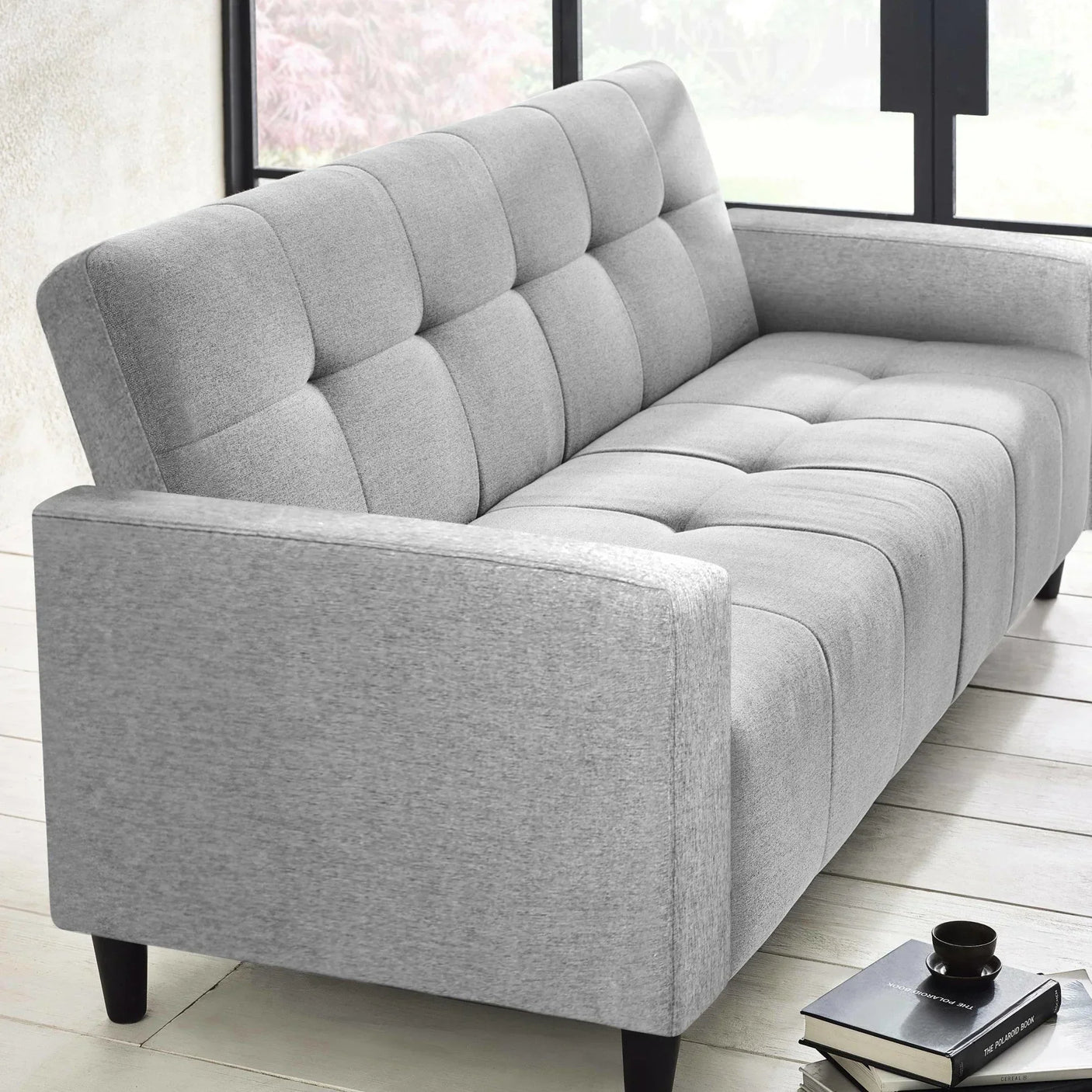 Light grey fabric sofa with tufted back and seat in modern living room, black legs