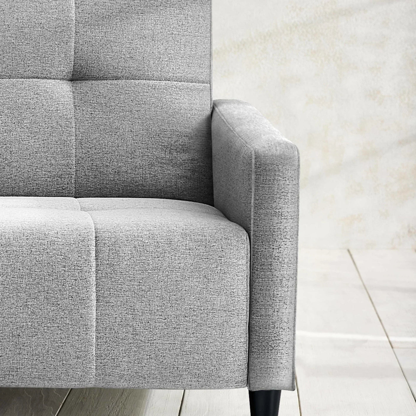 Light grey fabric sofa with square stitching and black wooden legs, partial armrest view