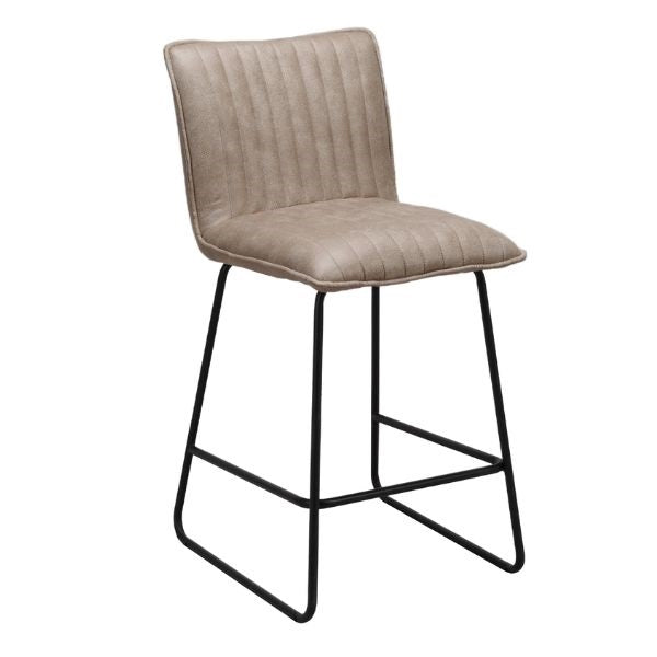 A modern counter stool with a light taupe-beige padded seat and backrest featuring vertical channel tufting, supported by a black metal frame with a footrest.