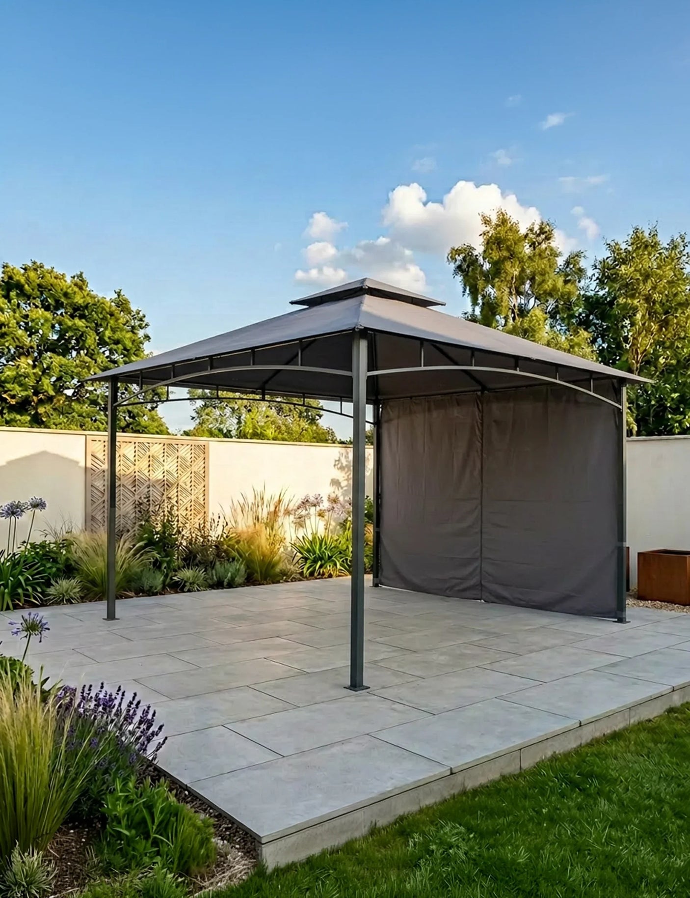 Grey metal garden gazebo with canopy and side panel on paved patio in landscaped yard