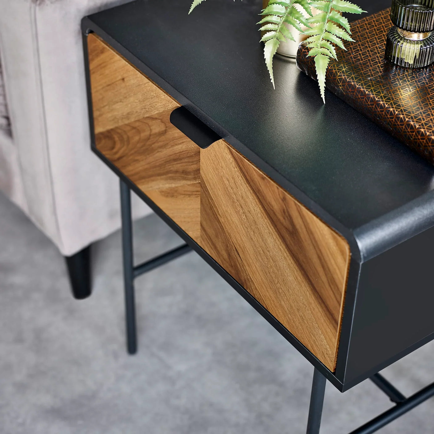 Modern side table with black top and chevron wood drawer beside grey sofa
