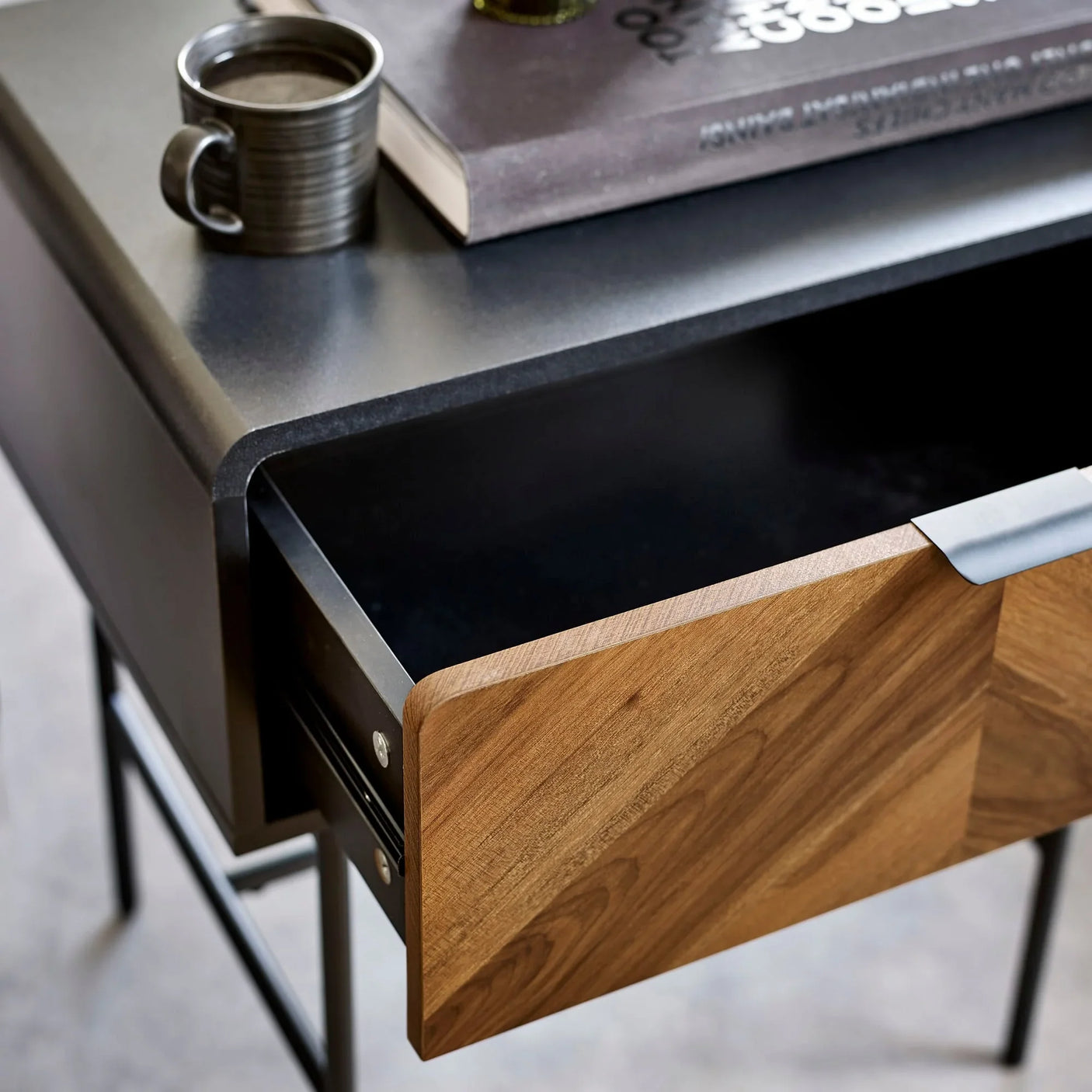 Modern black metal desk with open wood drawer, ceramic mug, and book on tabletop