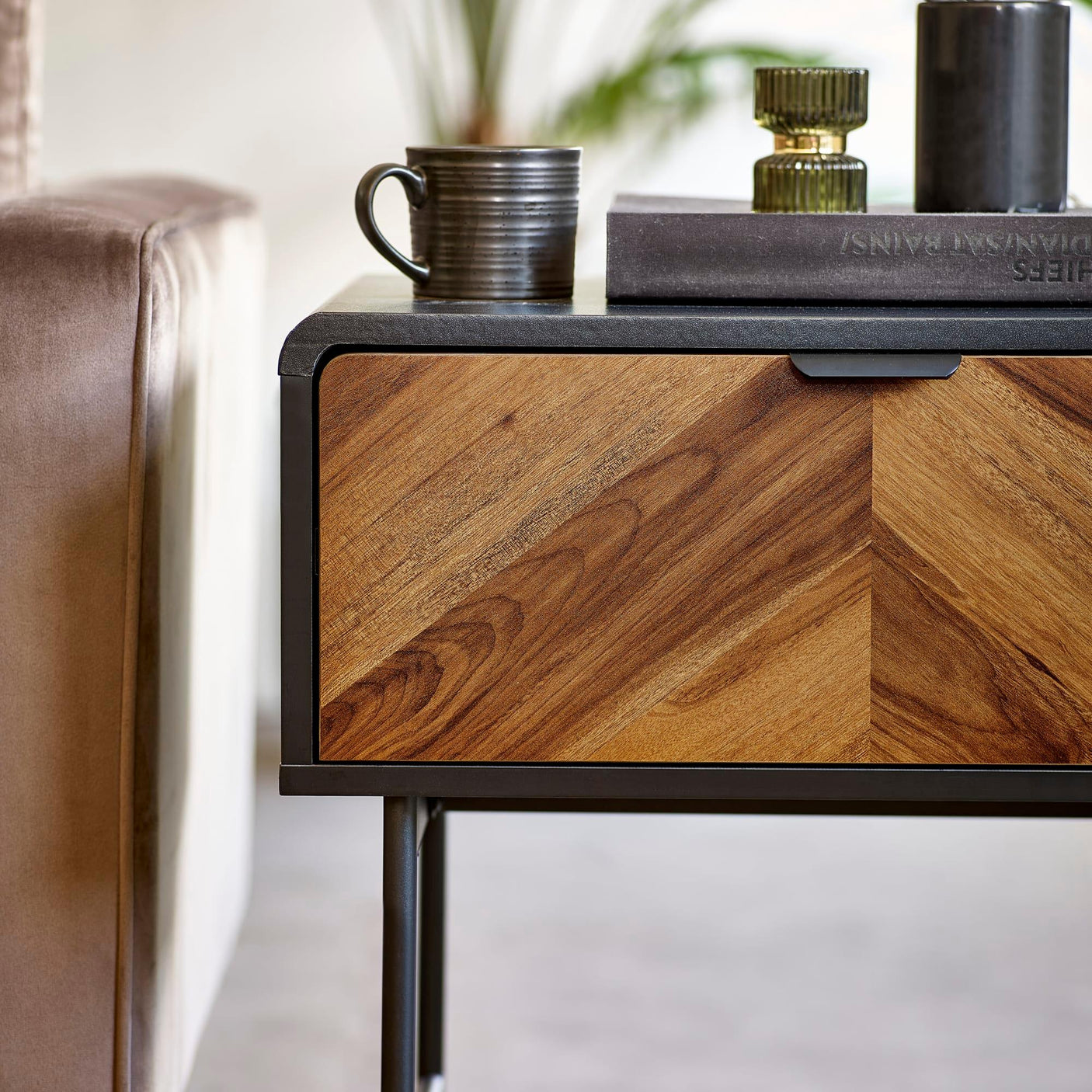 Wooden bedside table with chevron drawer detail and black frame beside a beige sofa