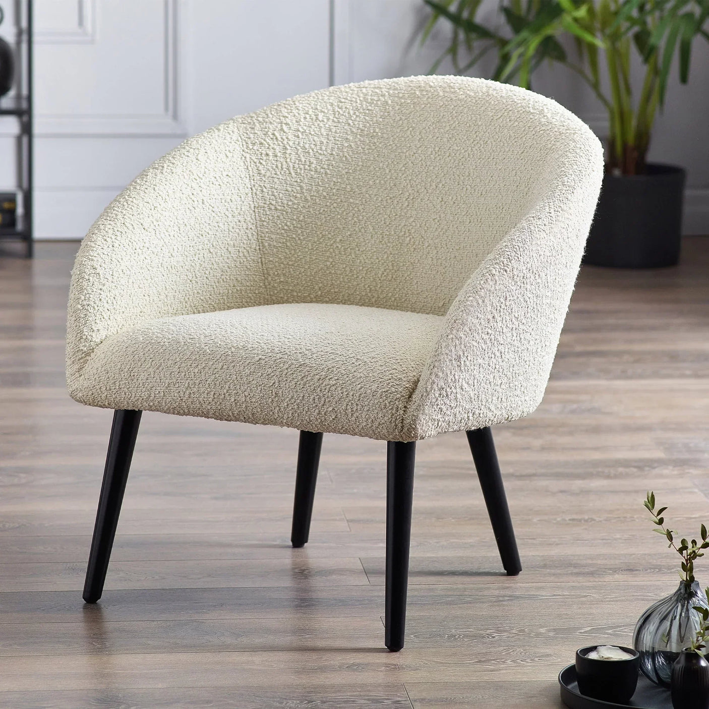 Cream boucle accent chair with curved backrest and black legs on wood floor