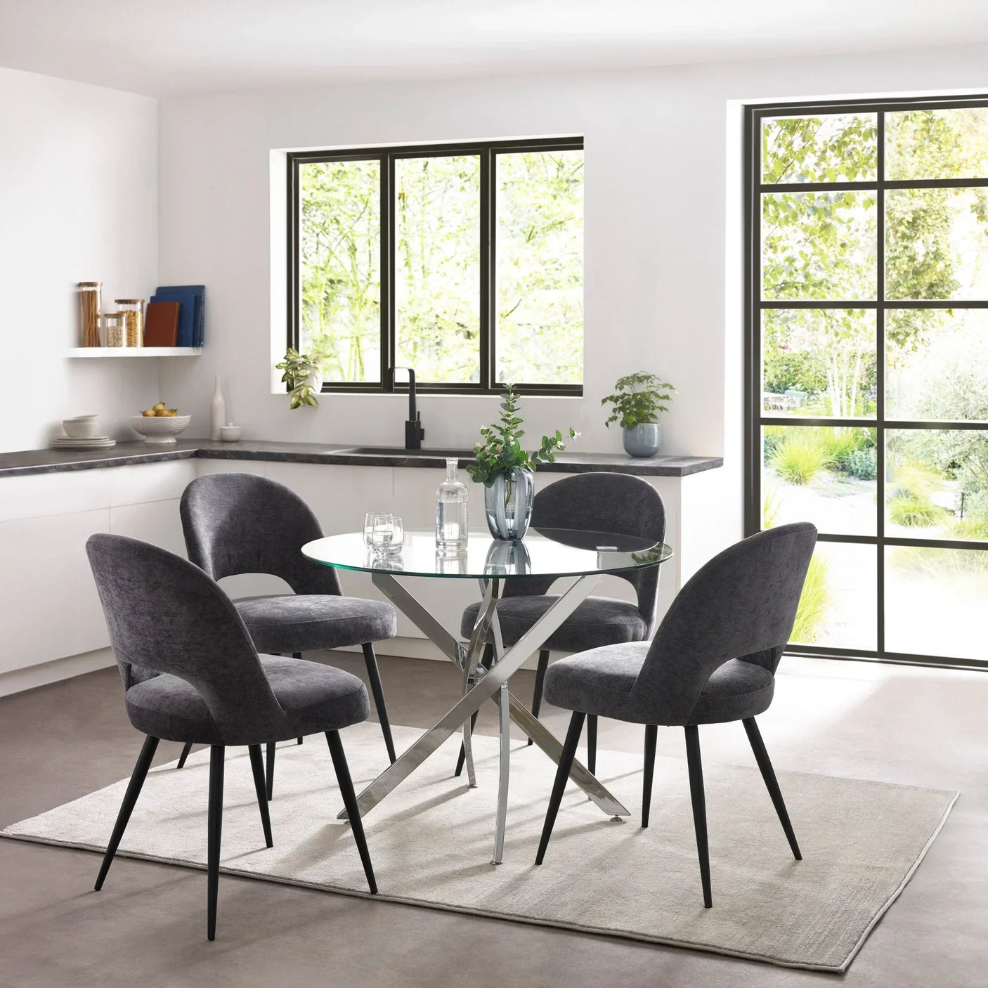 Round glass dining table with chrome base and four dark grey velvet chairs in modern kitchen