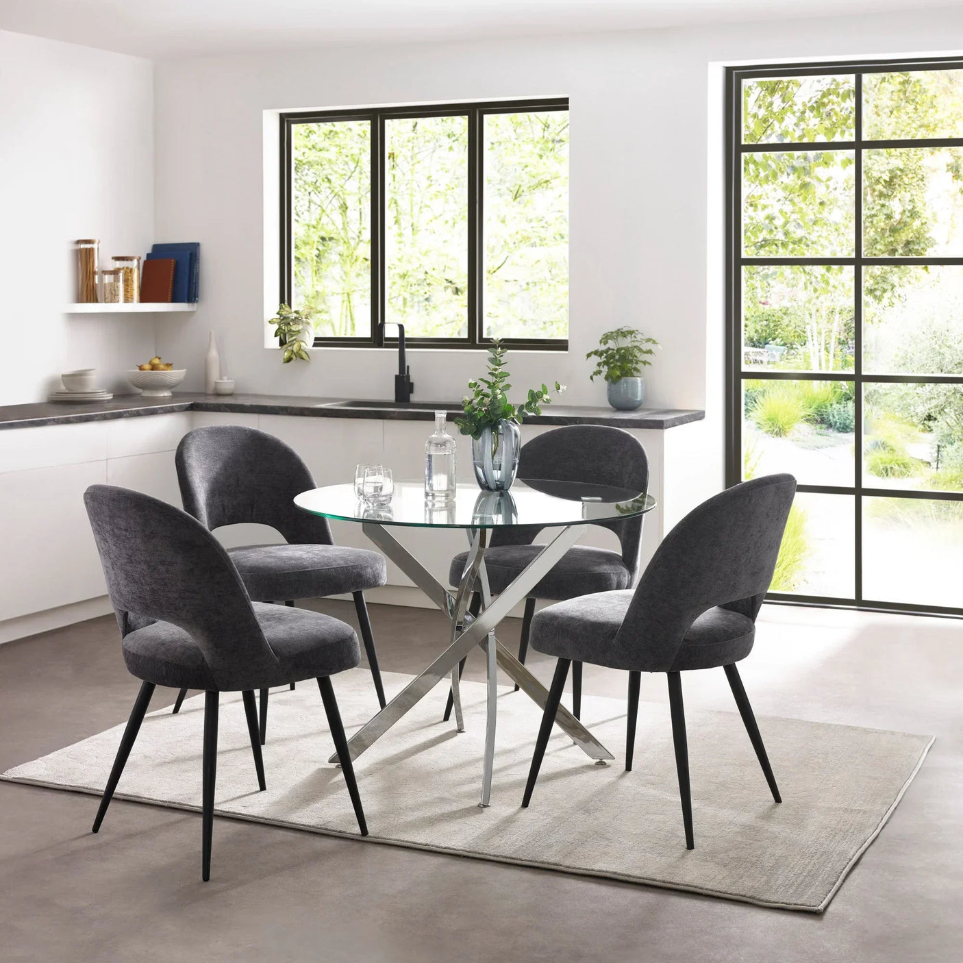 Round glass dining table with chrome legs and four grey chairs in modern kitchen setting