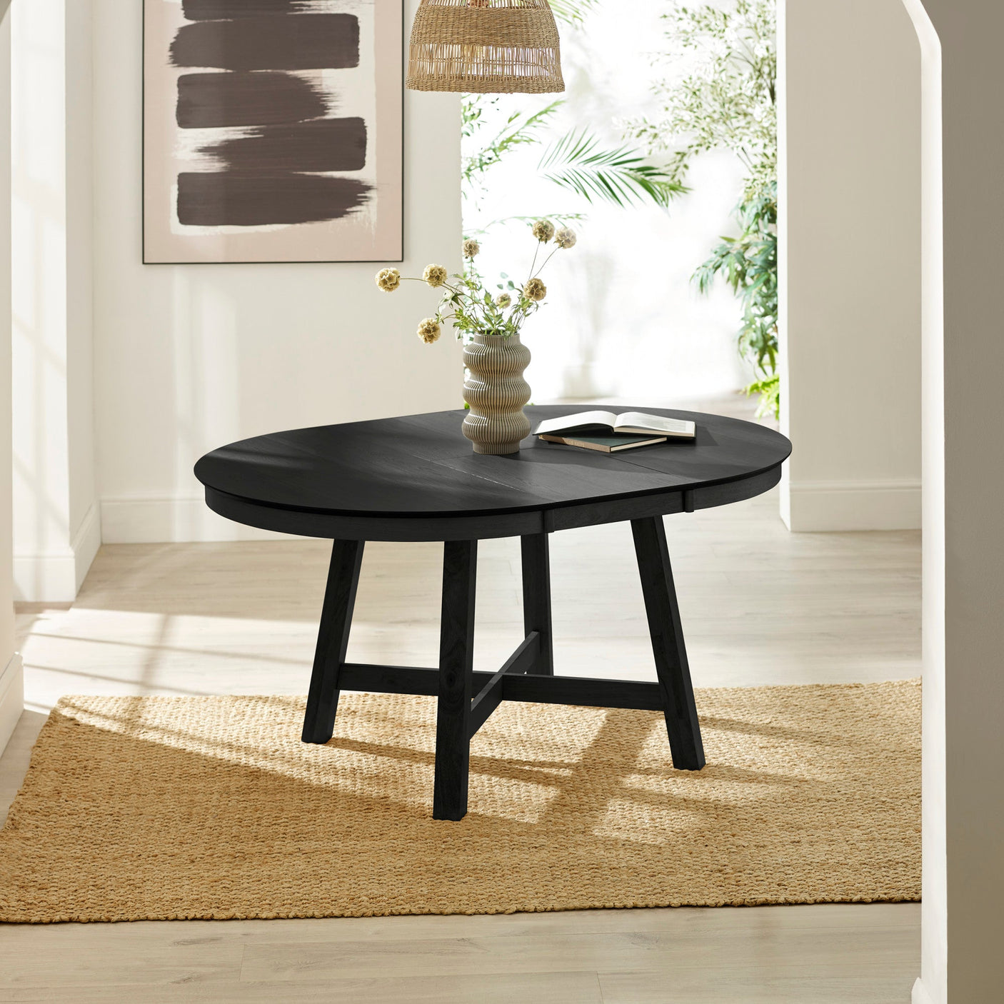 Extended black round wooden dining table with books and vase on top in bright room