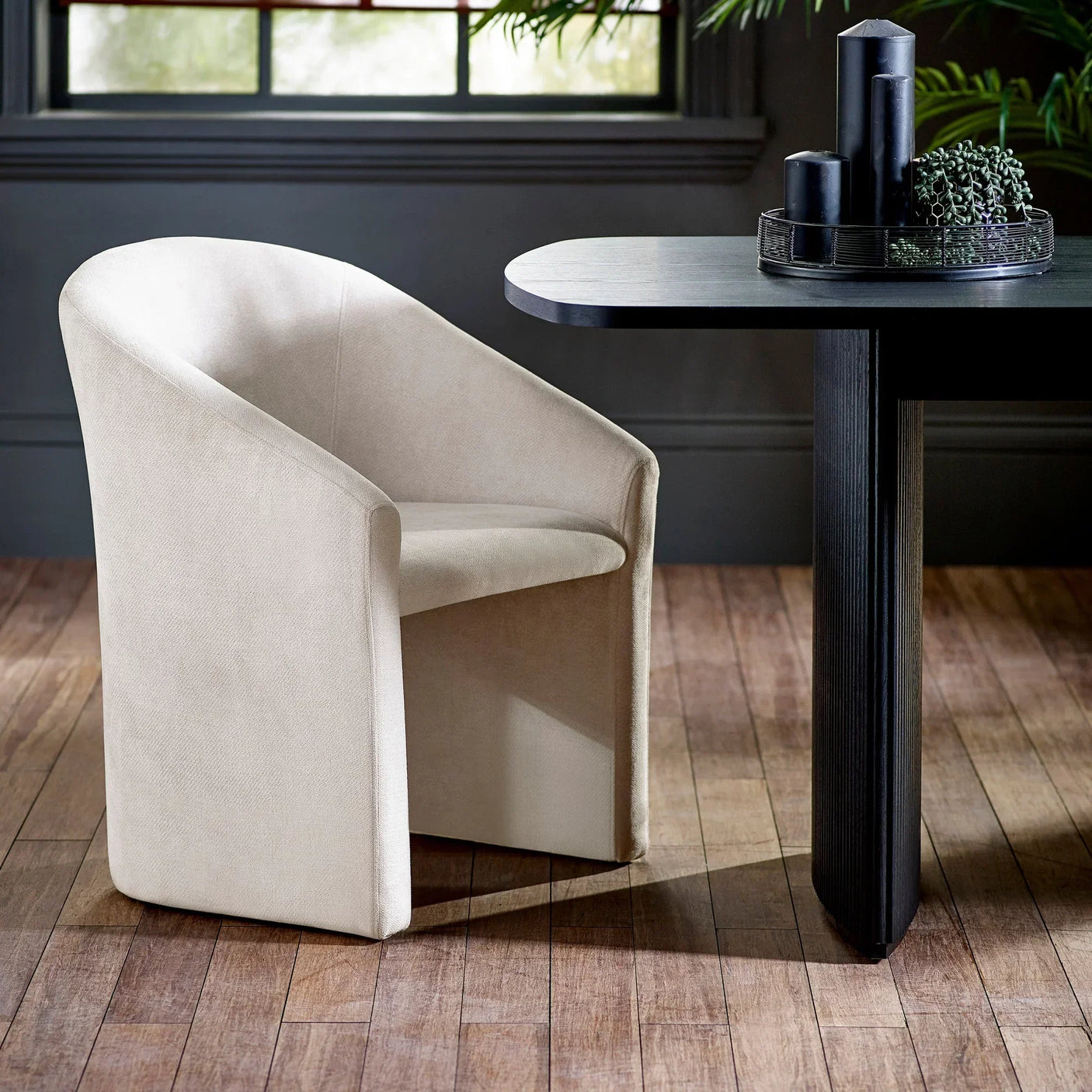 Beige fabric dining chair with curved back next to black rectangular dining table on wood floor