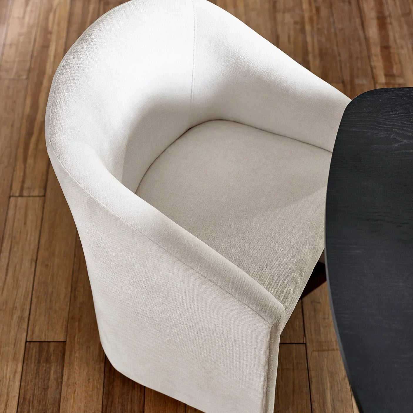 Cream upholstered dining chair with curved back next to dark wood table on wooden floor