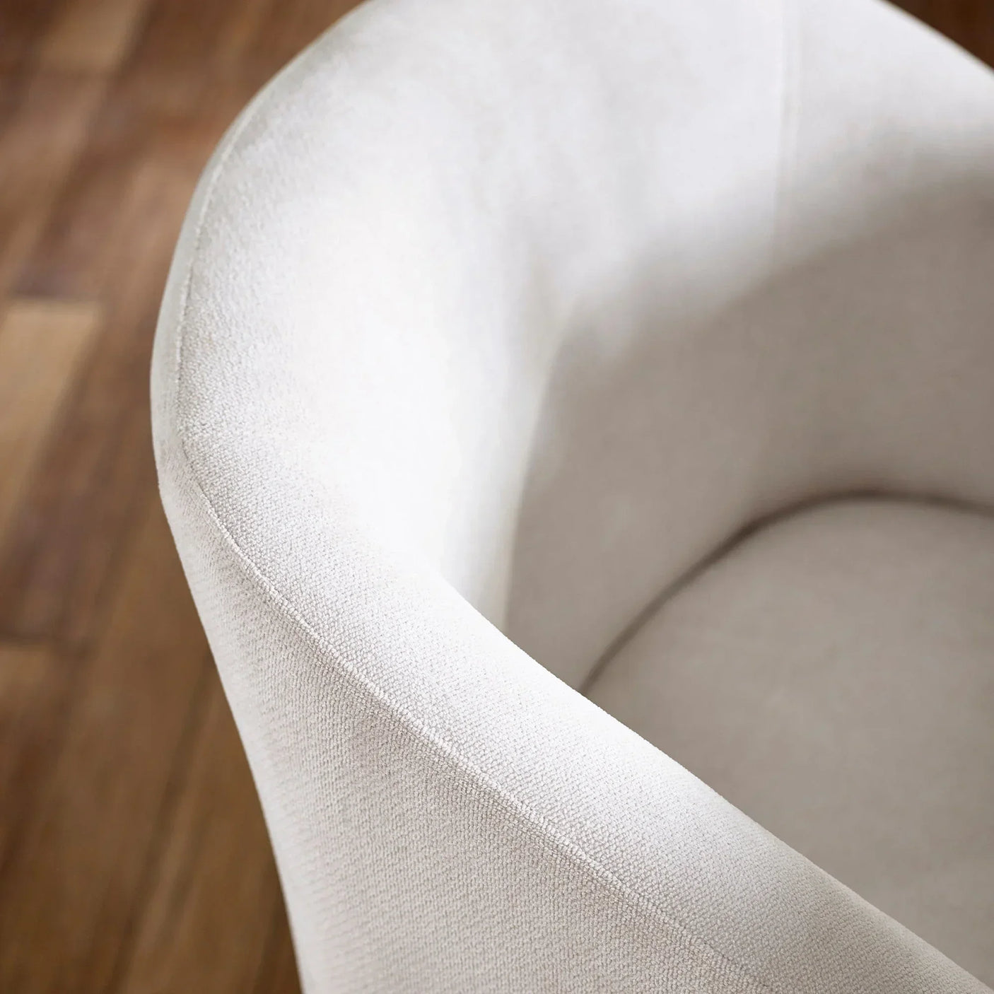 Closeup of cream upholstered armchair with curved backrest on wooden floor