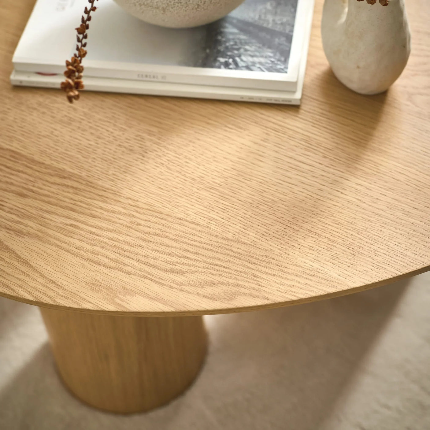 Round oak coffee table with books and ceramic decor on light carpet