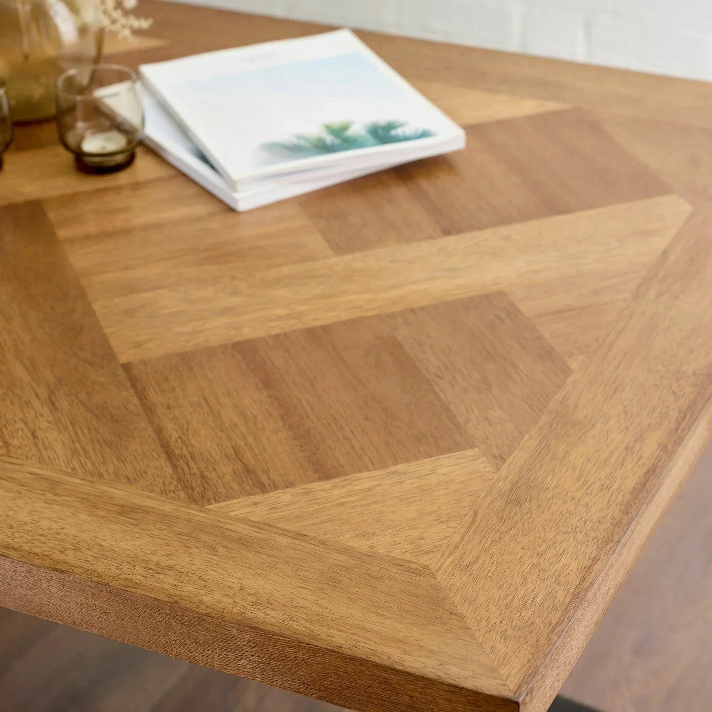 Close-up of wooden dining table with chevron pattern top, glassware and books on surface