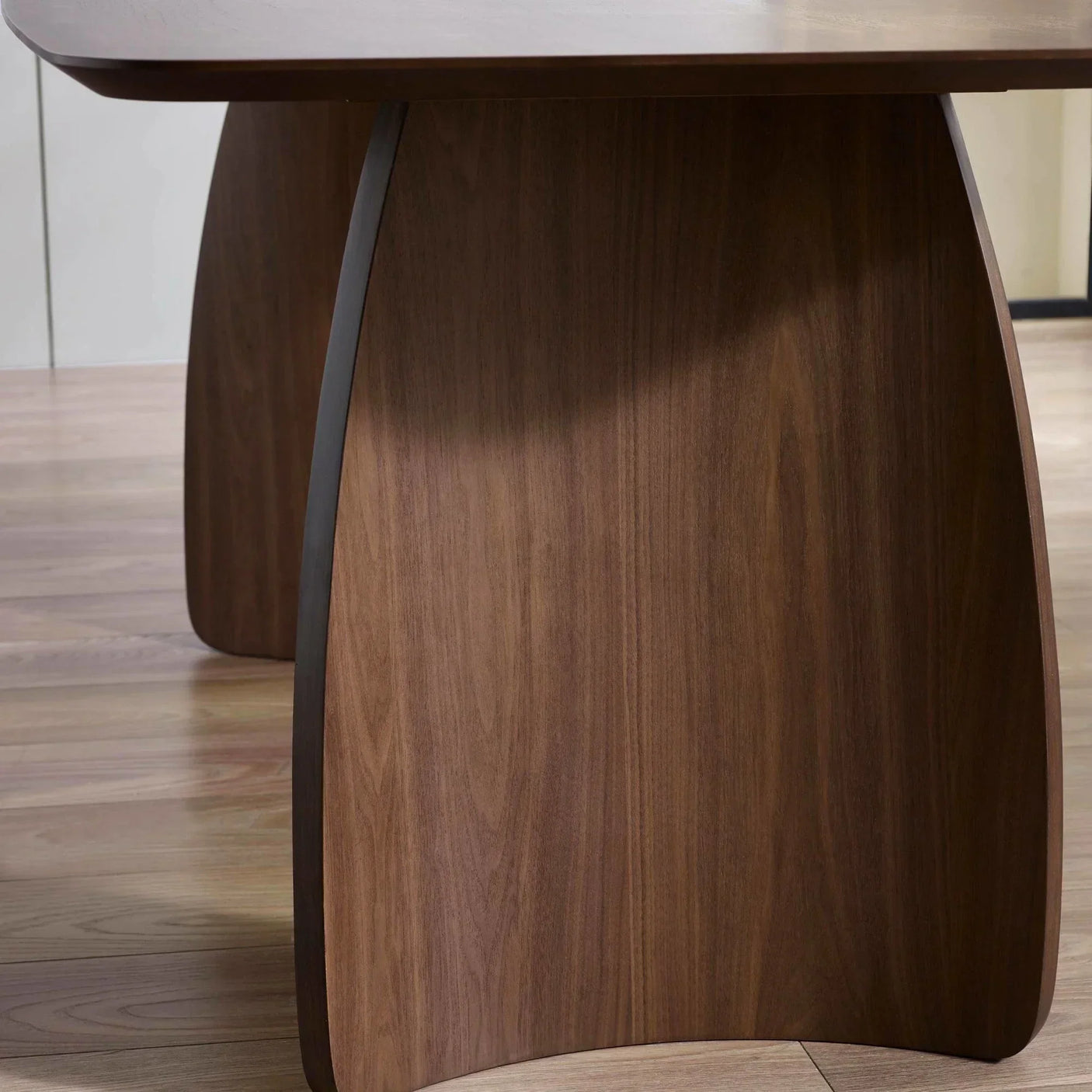 Walnut dining table base with curved wood grain detail on hardwood floor
