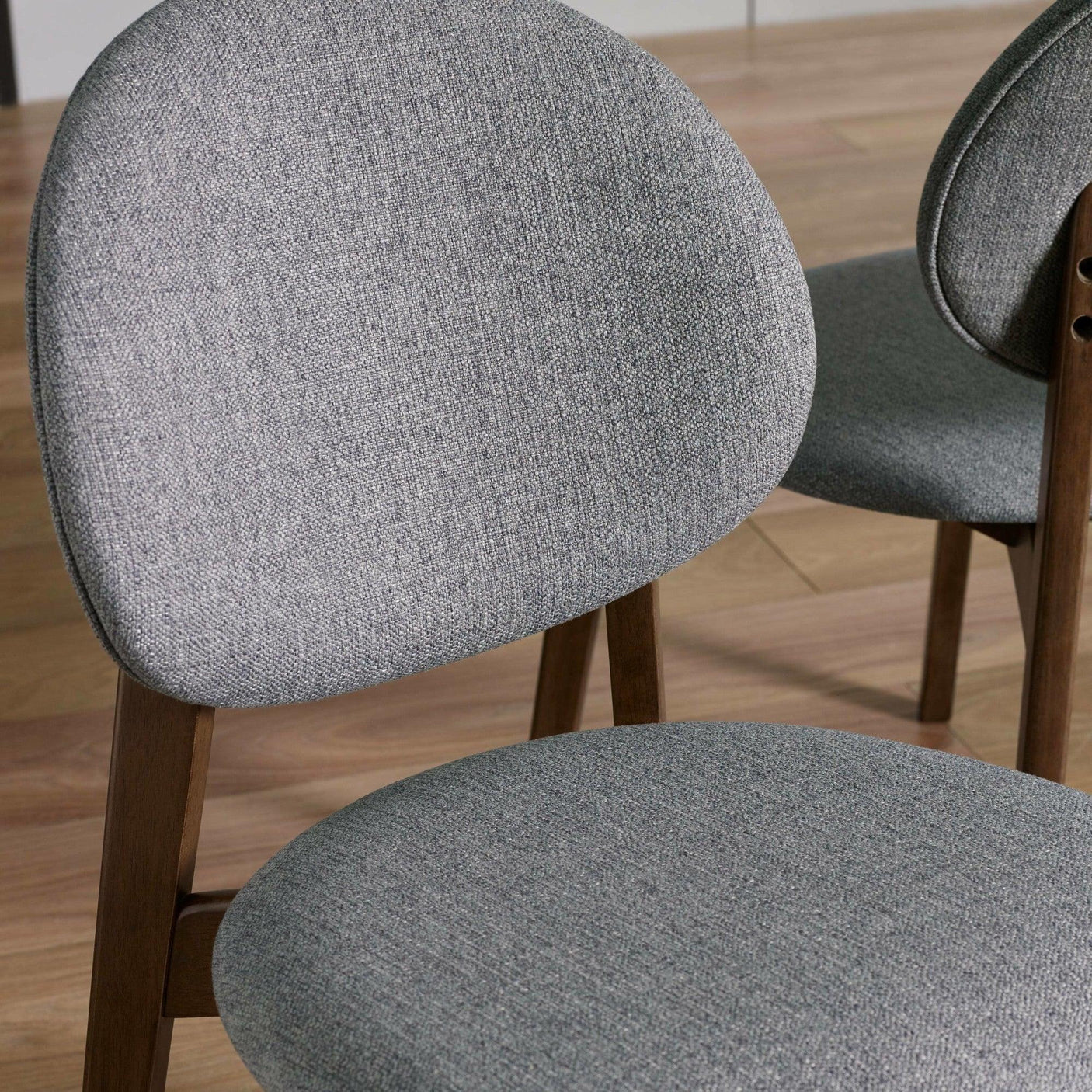 Grey fabric dining chairs with rounded backs and wooden legs on light wood flooring