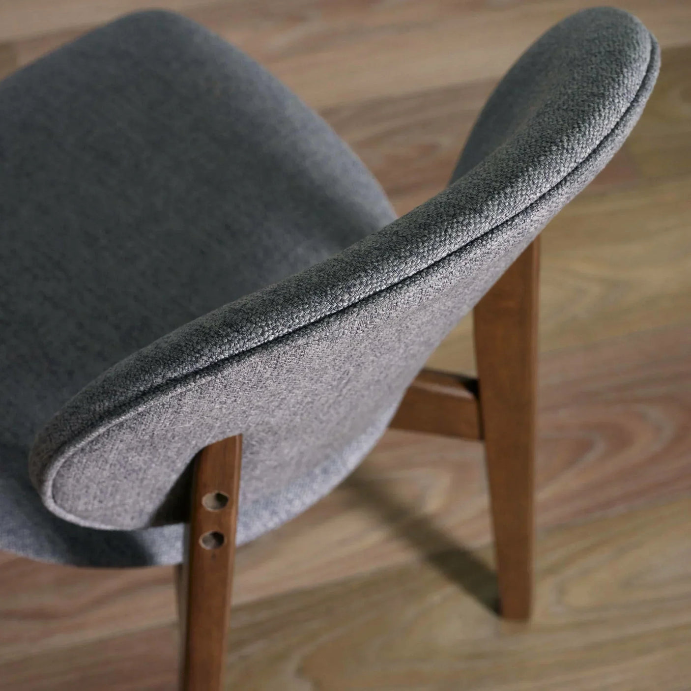 Grey fabric dining chair with curved backrest and wooden legs on light wood floor