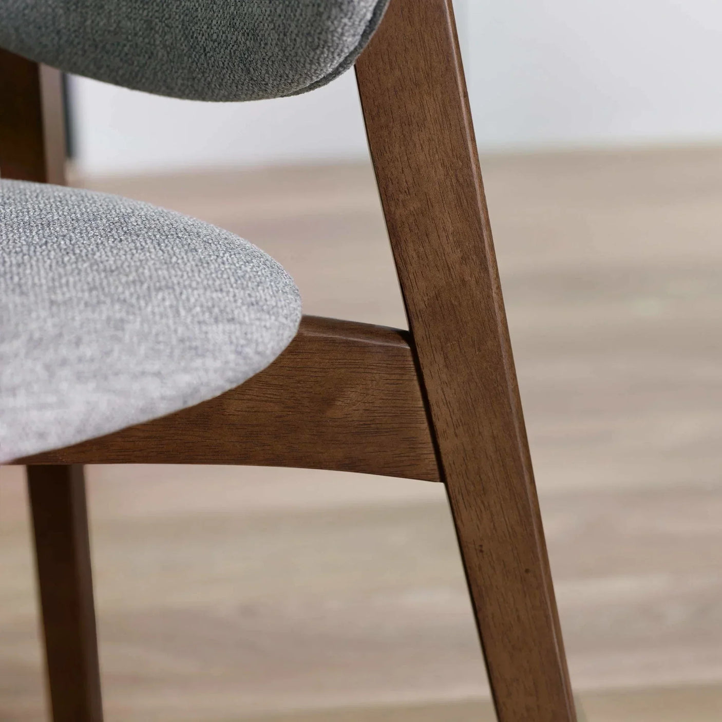 Closeup of dining chair with grey fabric seat and walnut wood frame