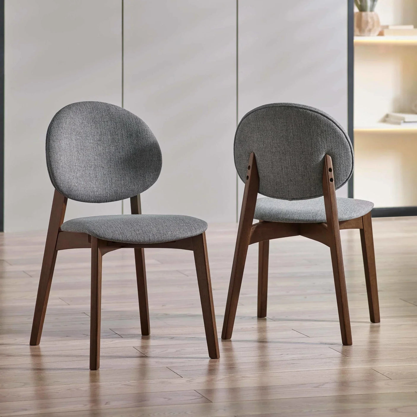Pair of grey upholstered dining chairs with wooden legs on light wood floor