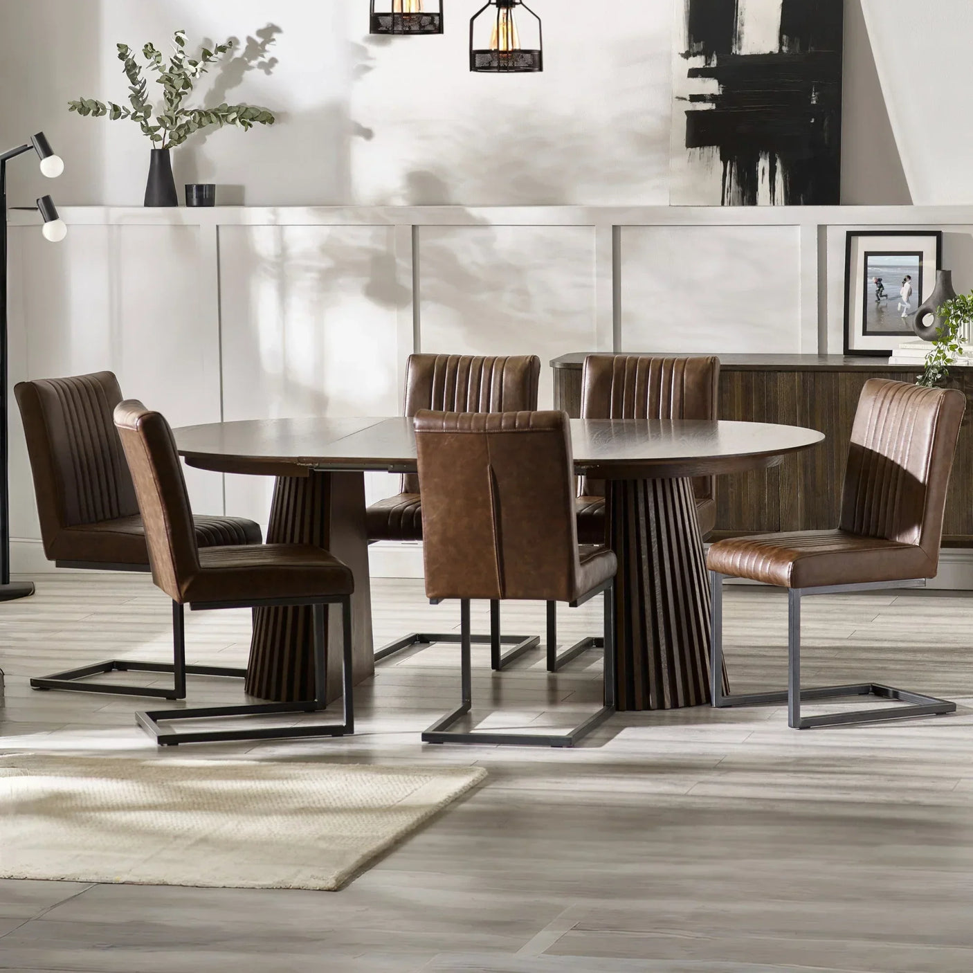 Round wood dining table with brown leather chairs in modern dining room setting