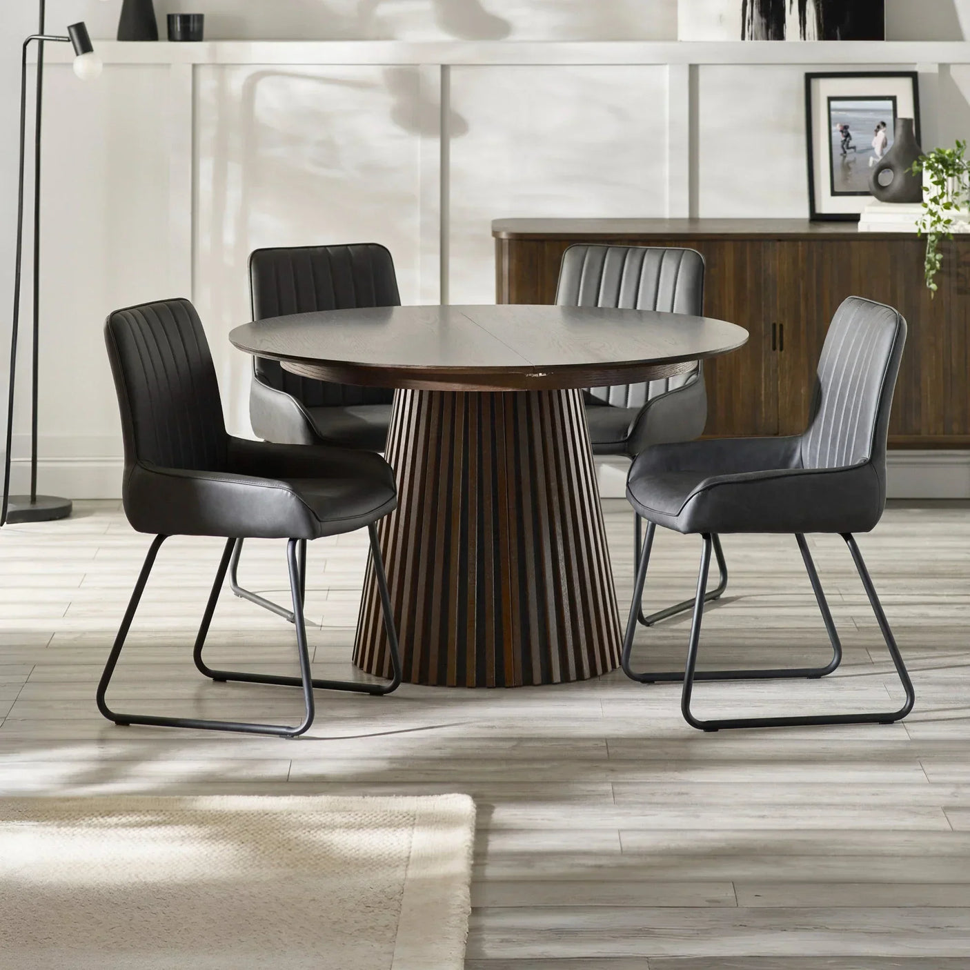 Round wood dining table with four black leather chairs in a modern dining room