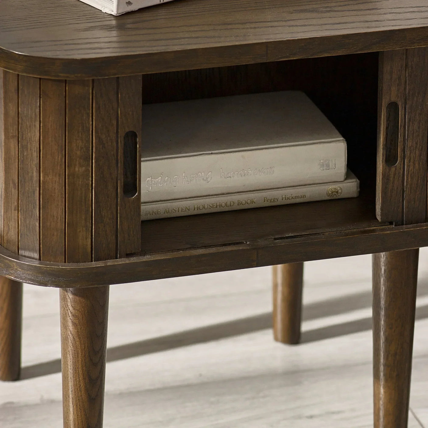 Dark wood side table with slatted sliding doors and open shelf displaying books
