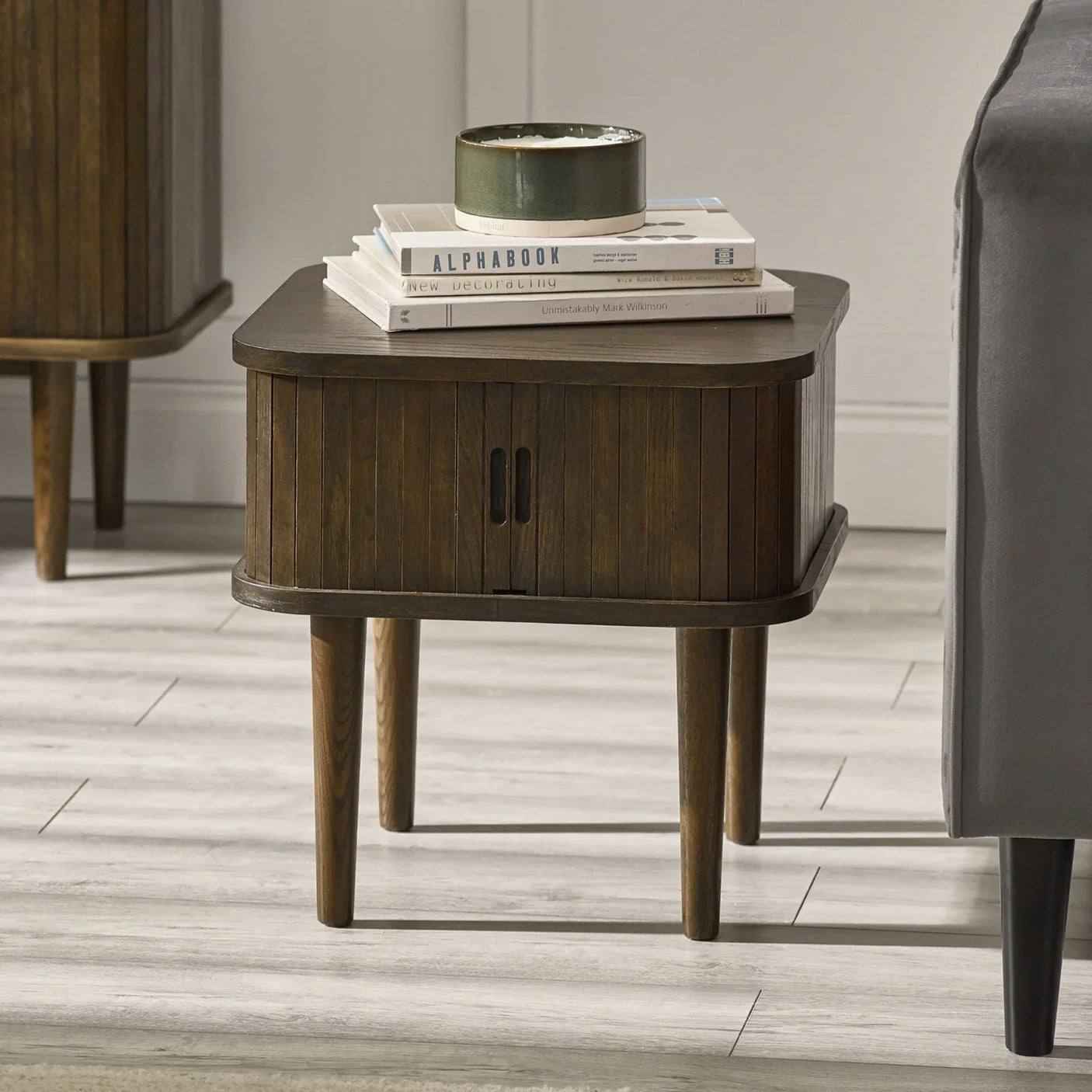 Dark wood bedside table with storage, books, and a ceramic bowl beside a sofa
