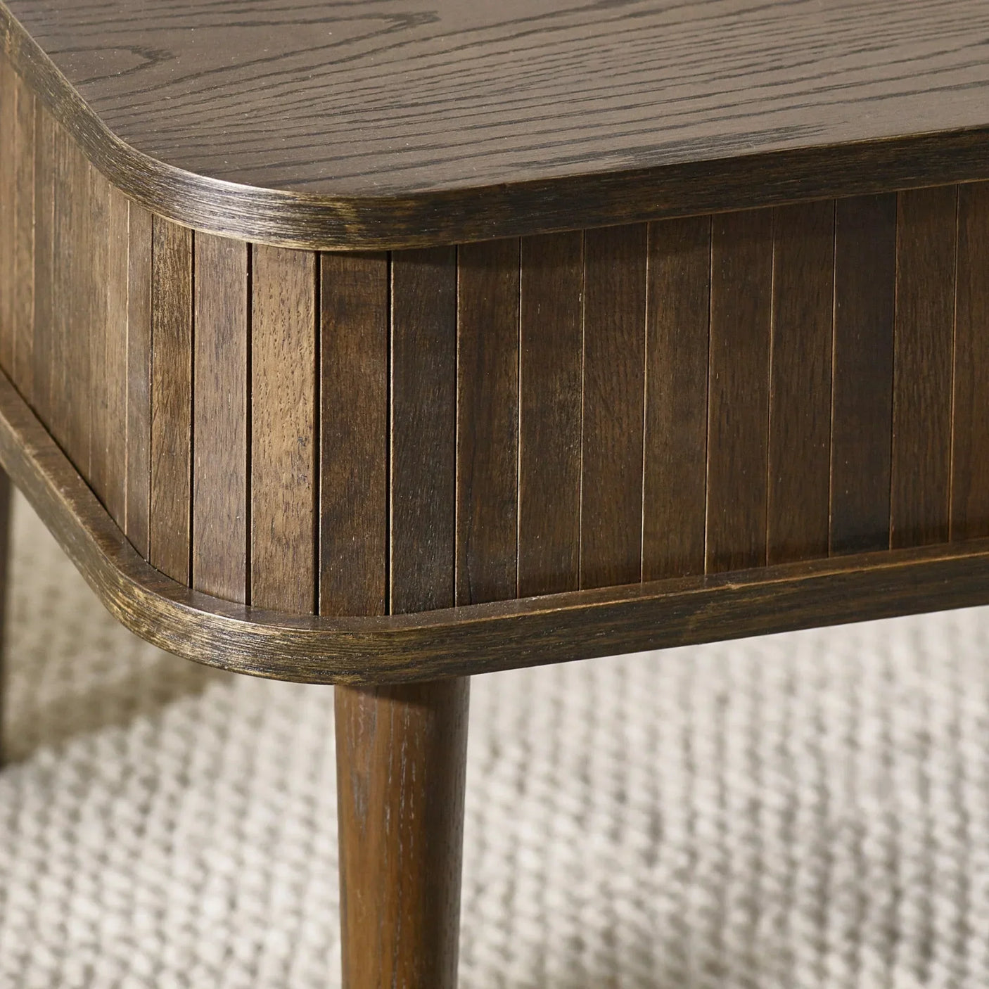 Dark wood coffee table with ribbed panel detail and rounded corner on textured rug