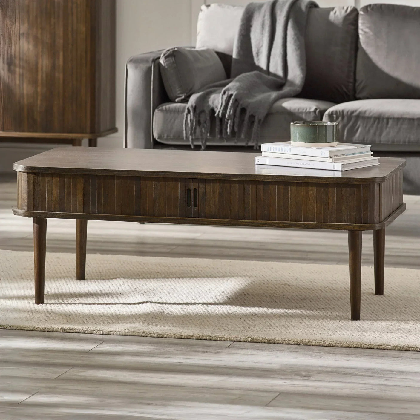 Rectangular dark wood coffee table with slim legs, books and bowl, in front of grey sofa