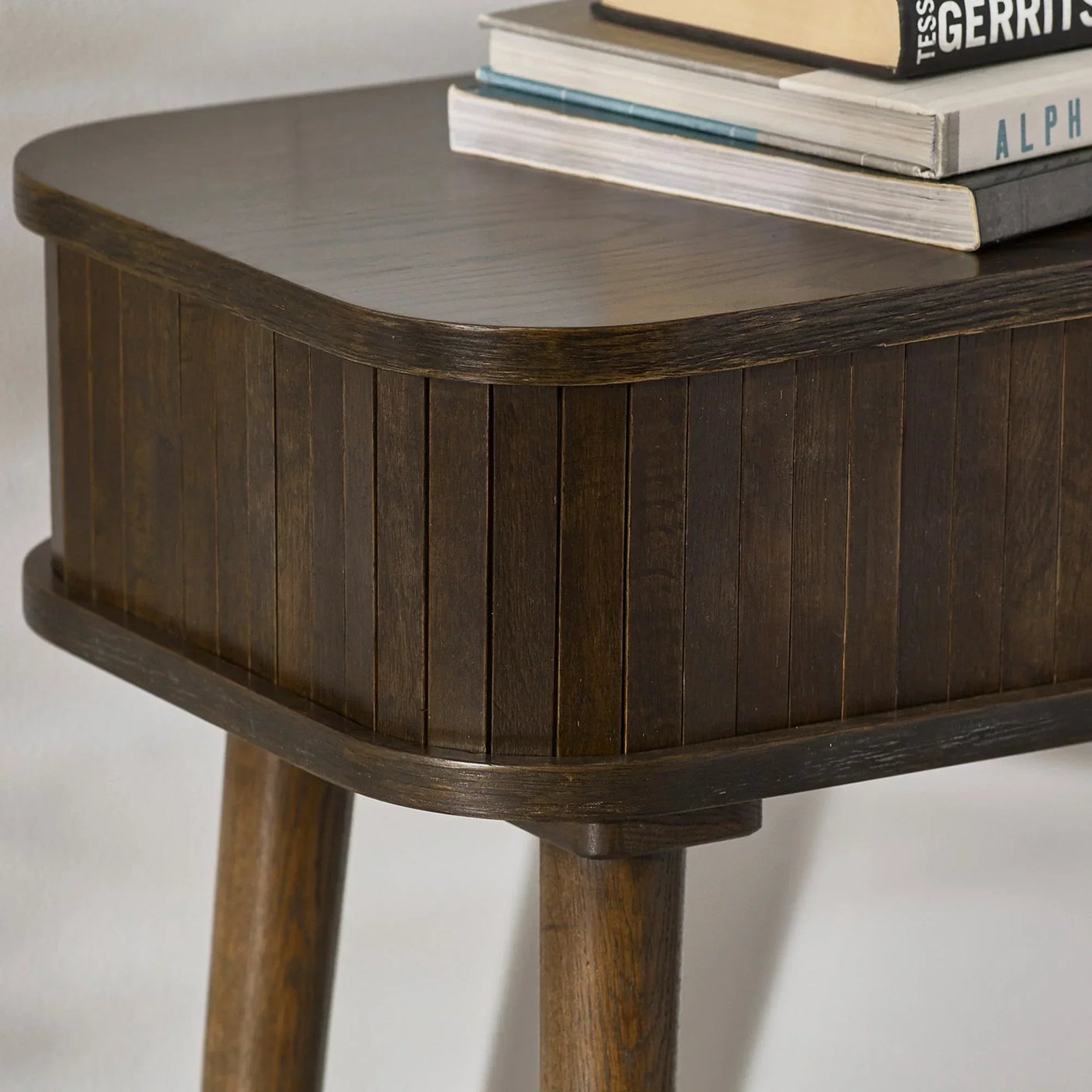 Dark wood bedside table with rounded edges and vertical panel detail, books stacked on top