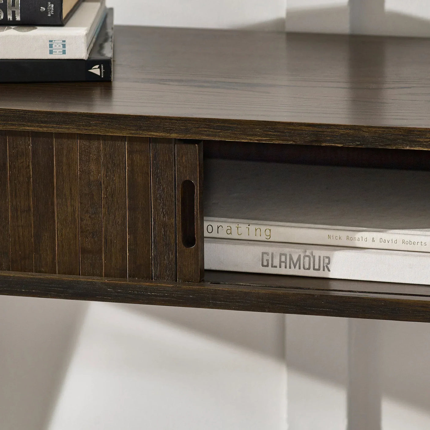 Dark wood TV unit shelf with sliding door and stacked books on top and inside compartment