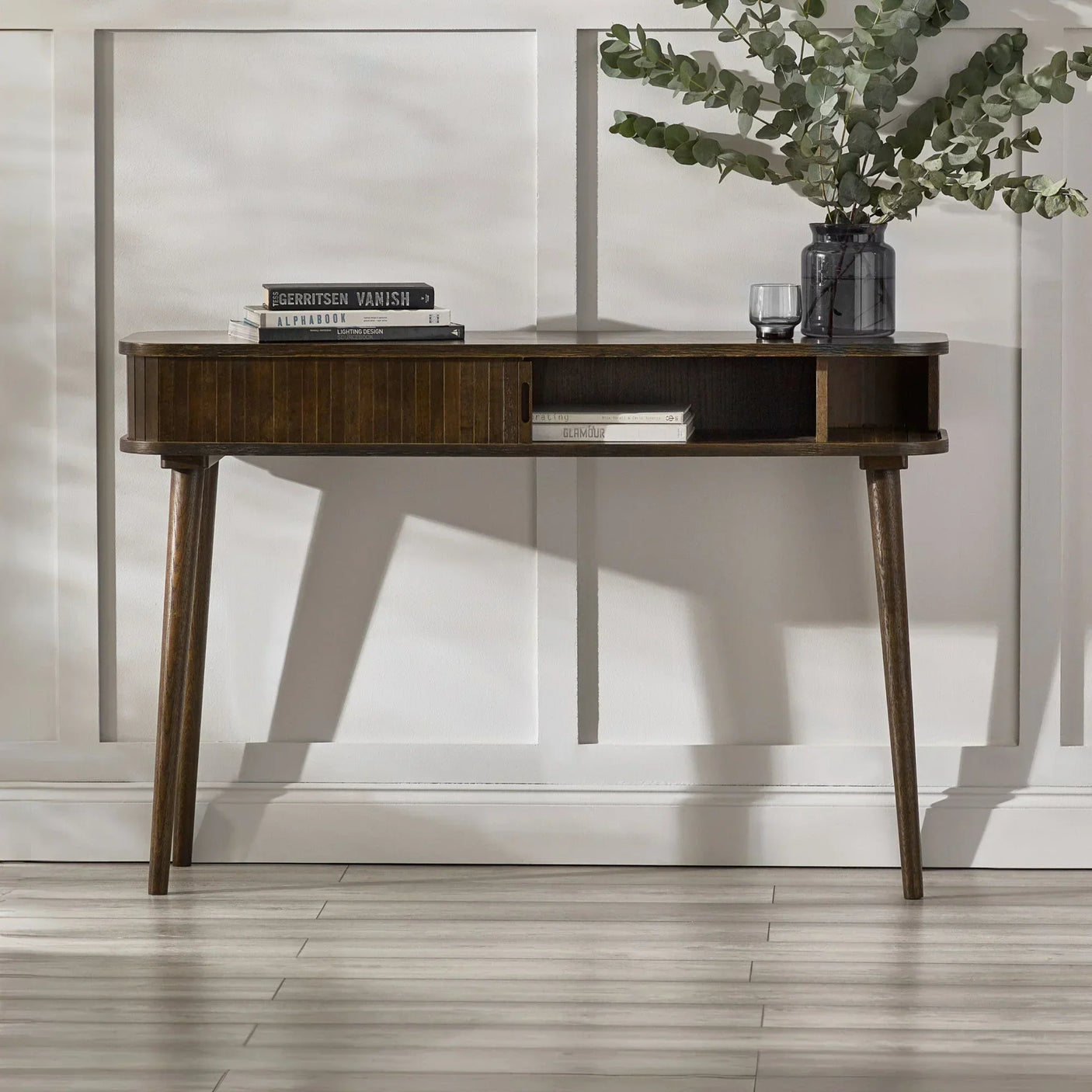 Mid-century wooden console table with books and vase in hallway setting