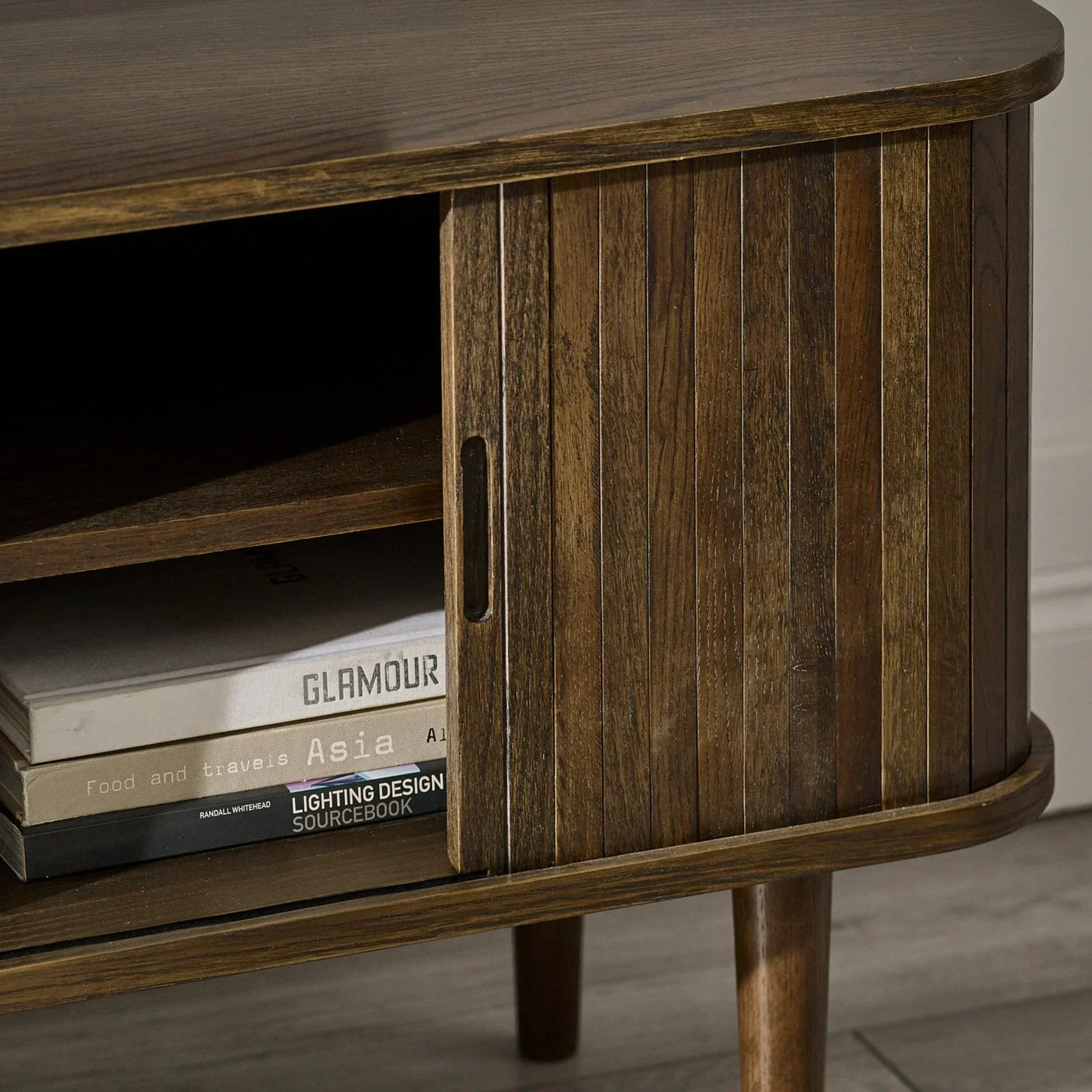 Dark wood TV unit with grooved sliding door, open shelf and four stacked books visible