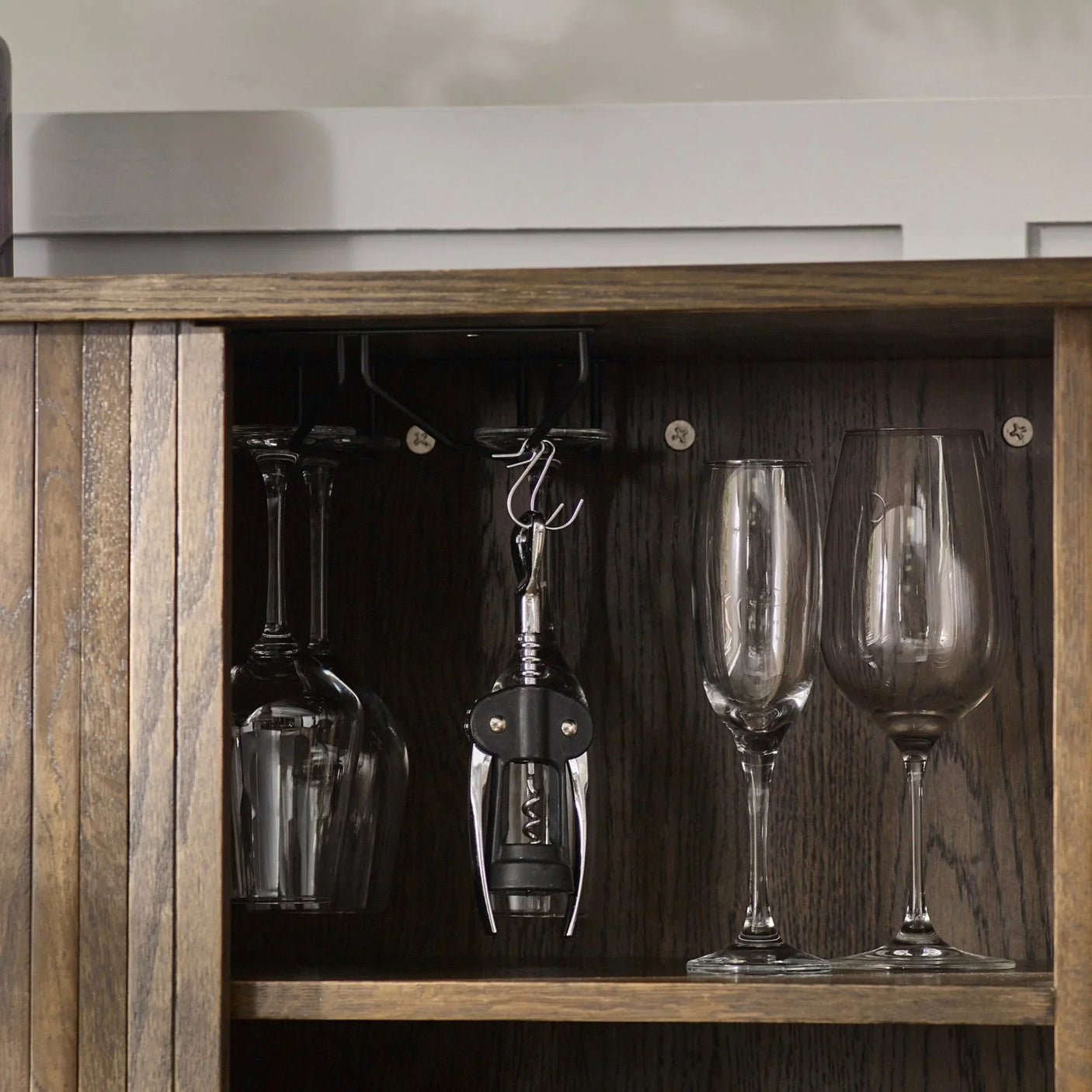 Wooden drinks cabinet interior with hanging wine glasses, corkscrew, and glassware display