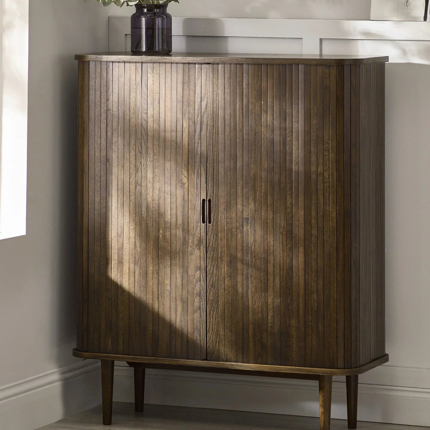Mid century wooden sideboard with vertical slat doors in corner of living room