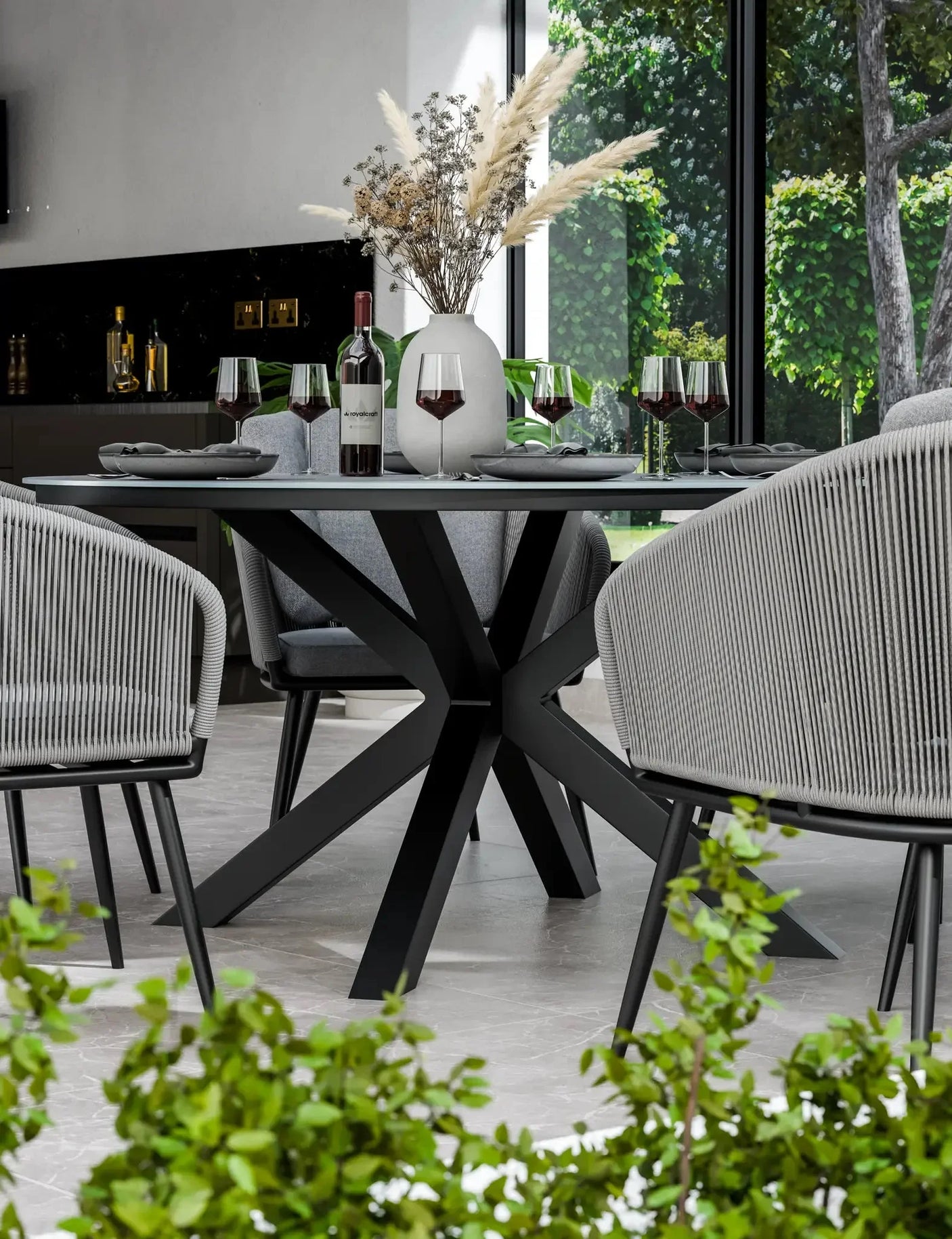 Modern black dining table with star-shaped base, grey chairs, and wine glasses in bright room