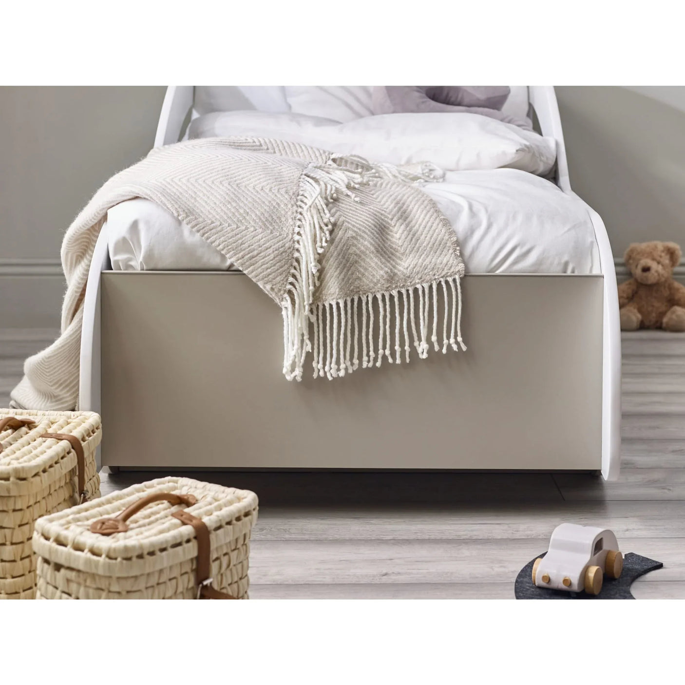 Modern single bed with white bedding, cream throw, and woven storage baskets on wood floor