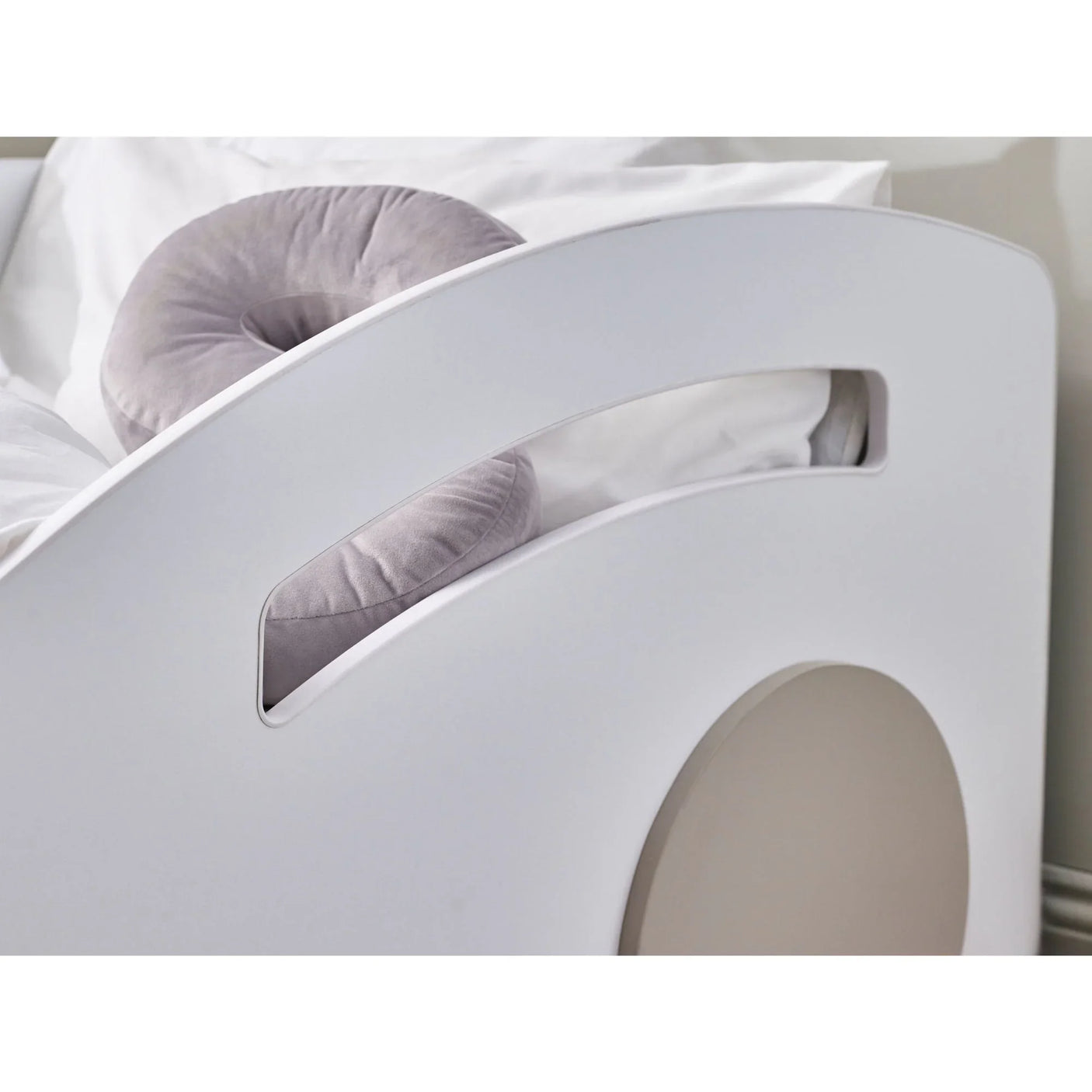 White bed frame with circular headboard detail and grey cushion, close-up view